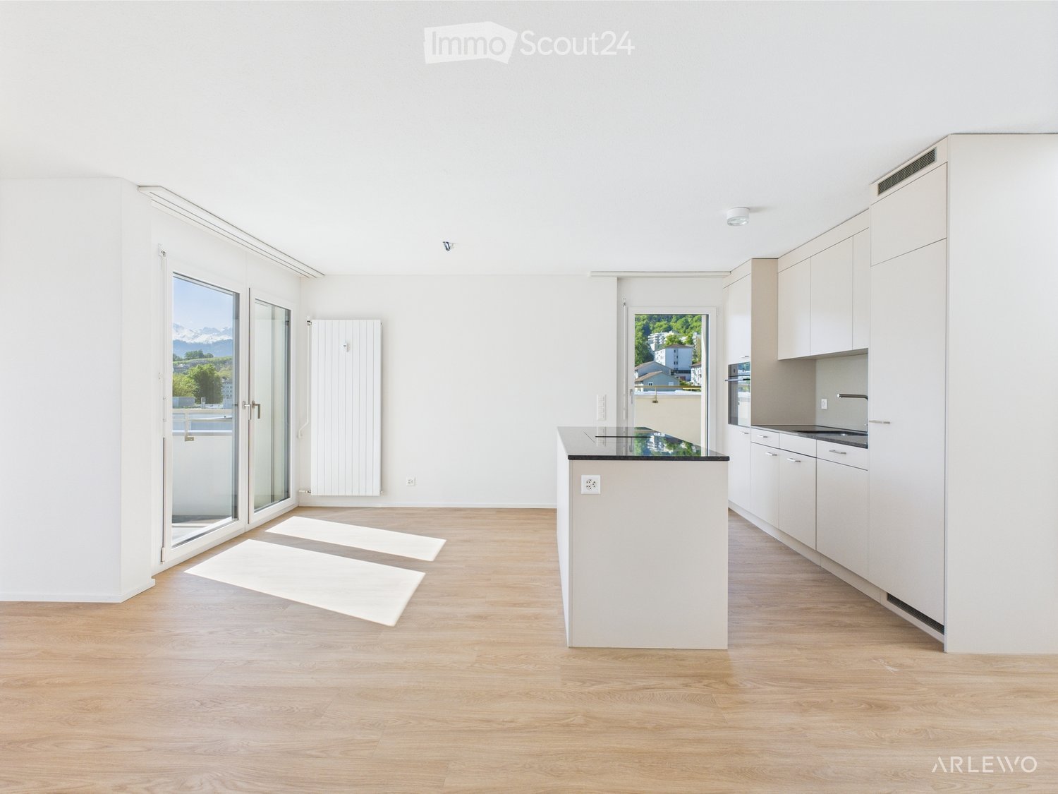 Open-plan kitchen and living area with light wood flooring, white cabinetry, and large windows offering a scenic view.