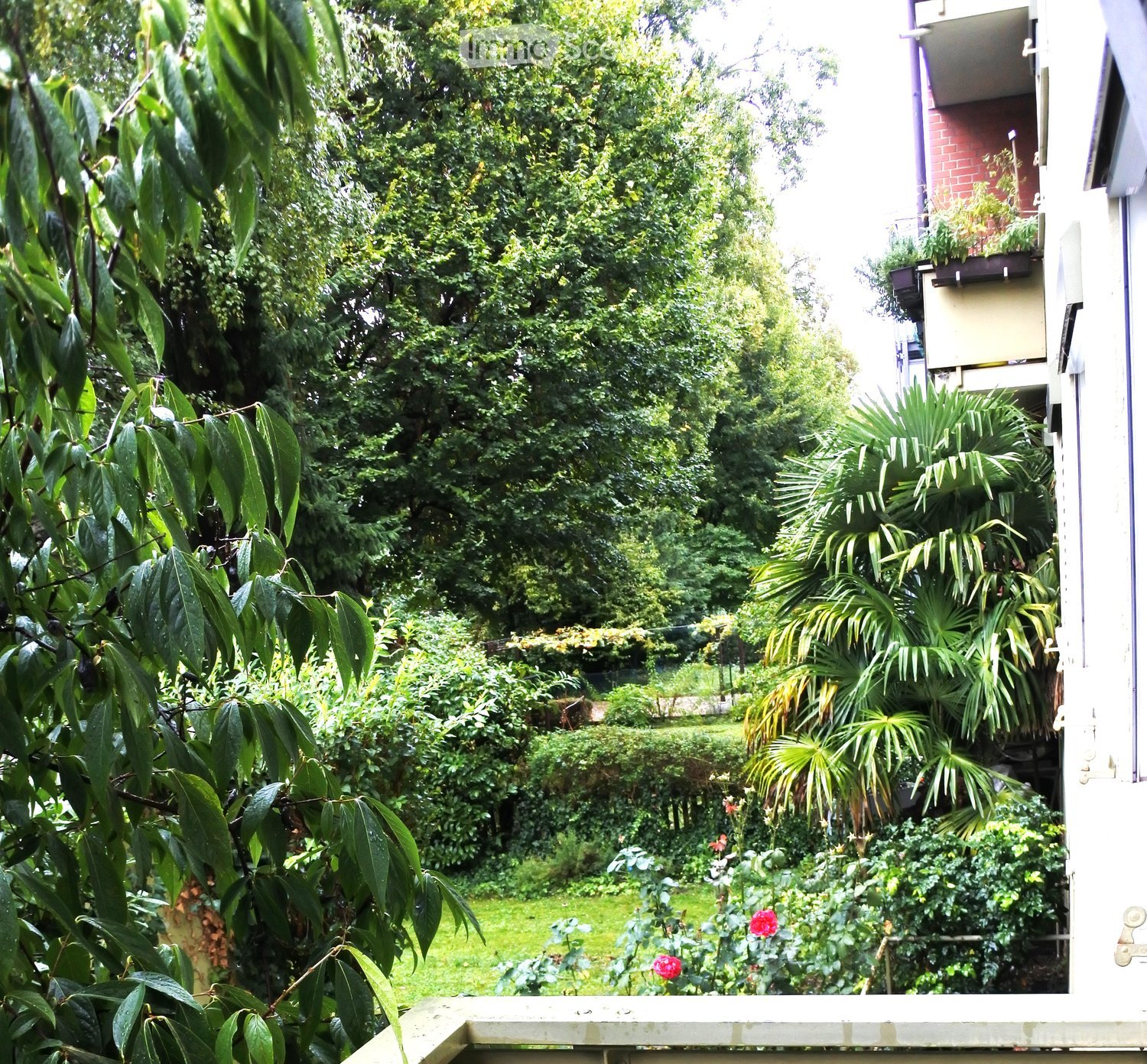 A lush garden with various plants, trees, and flowers, visible from a balcony or terrace area.