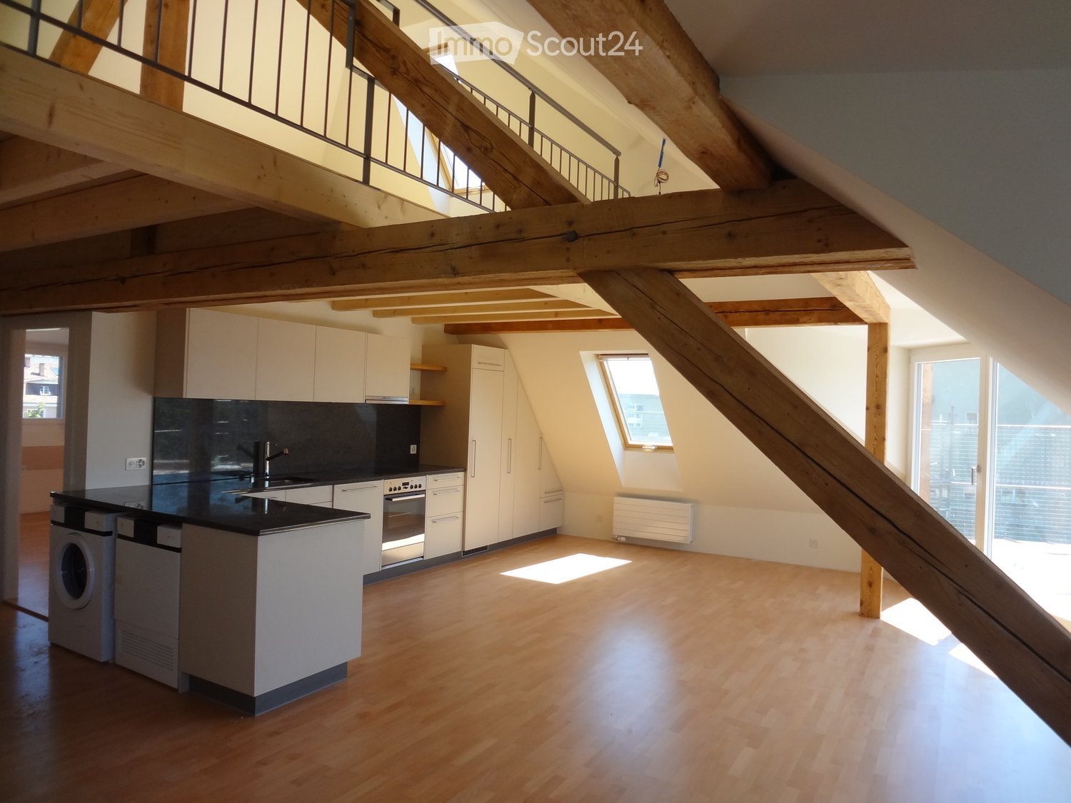 Modern kitchen with white cabinets, black countertops, stainless steel appliances, and wooden flooring. Features a staircase leading to an upper level.