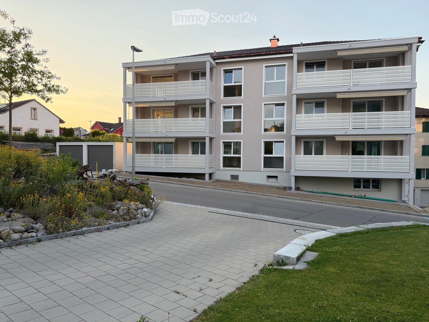 Modern two-story residential building with balconies, large windows, and a paved driveway.