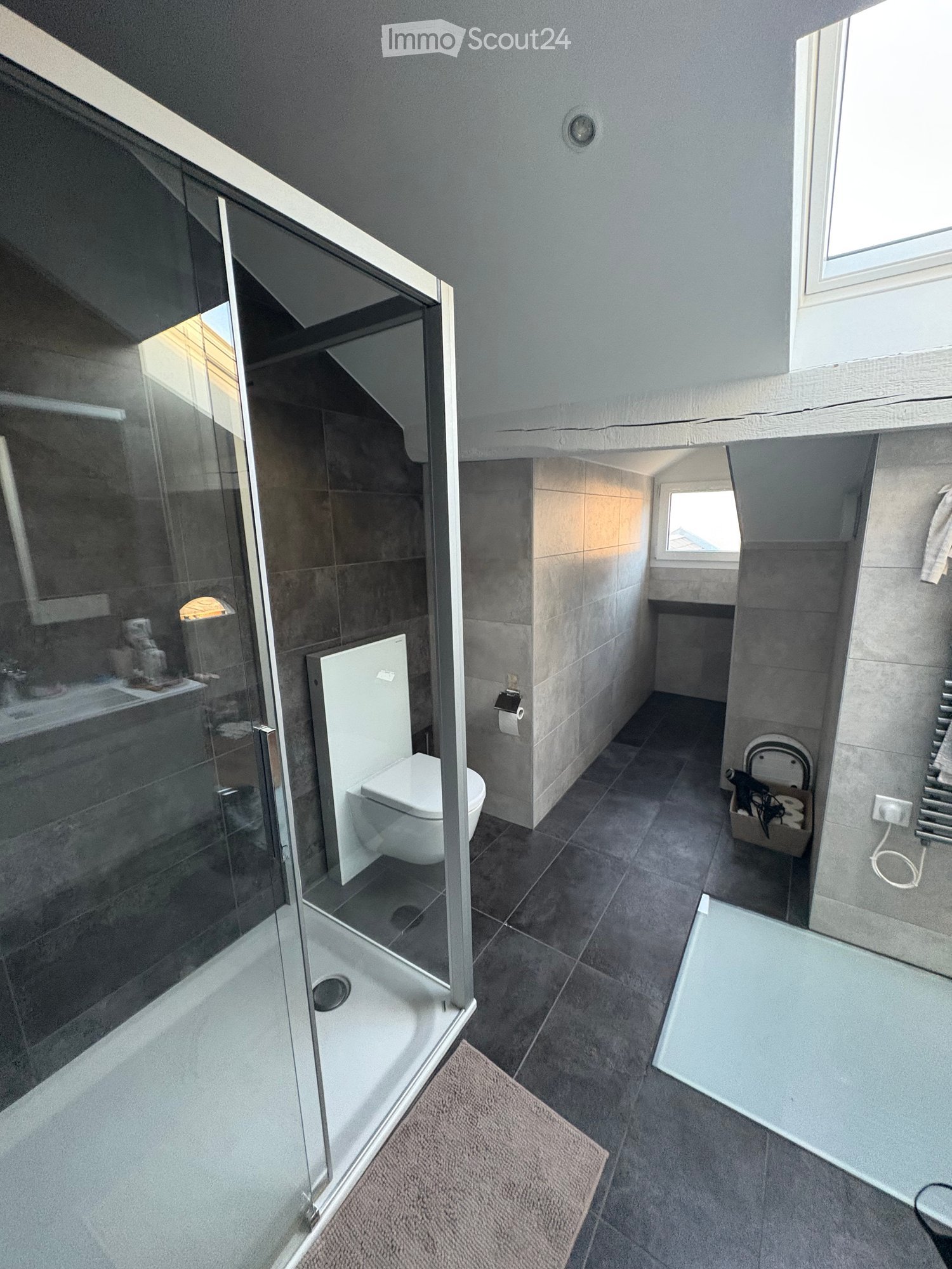 Modern bathroom with a glass-enclosed shower, toilet, sink, and towel rack. Features include a small window, a bathrobe, and a hair dryer on a shelf.
