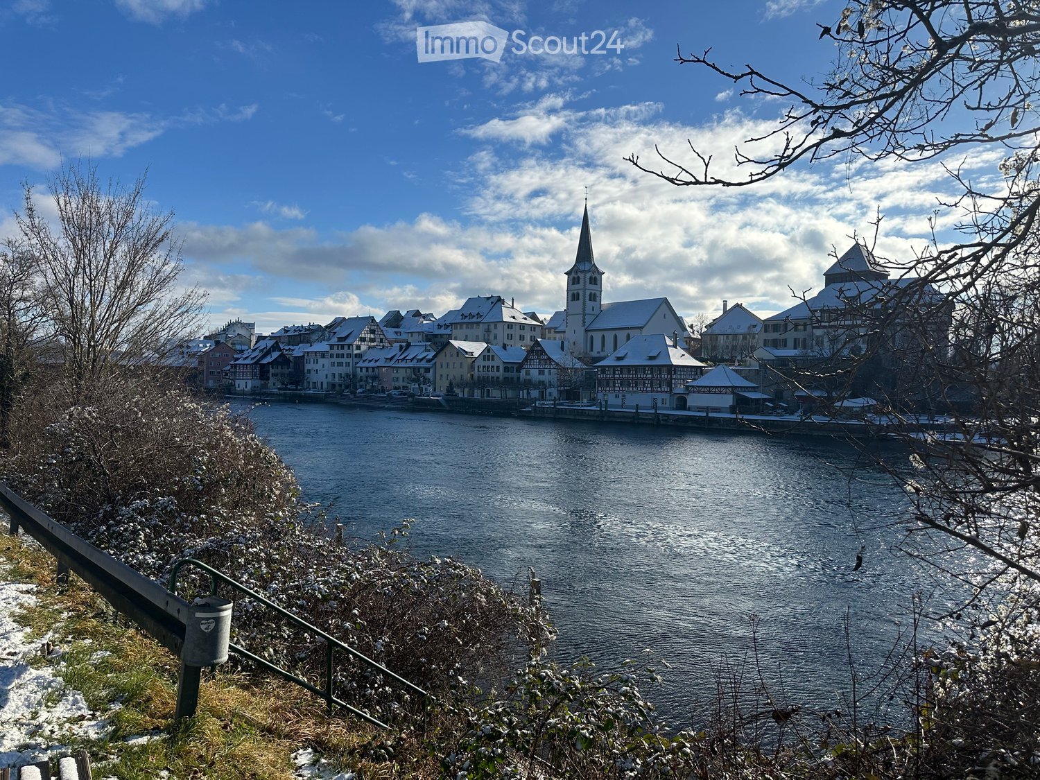 Scenic view of a town with a river, snow-covered buildings, and a church spire in the background.