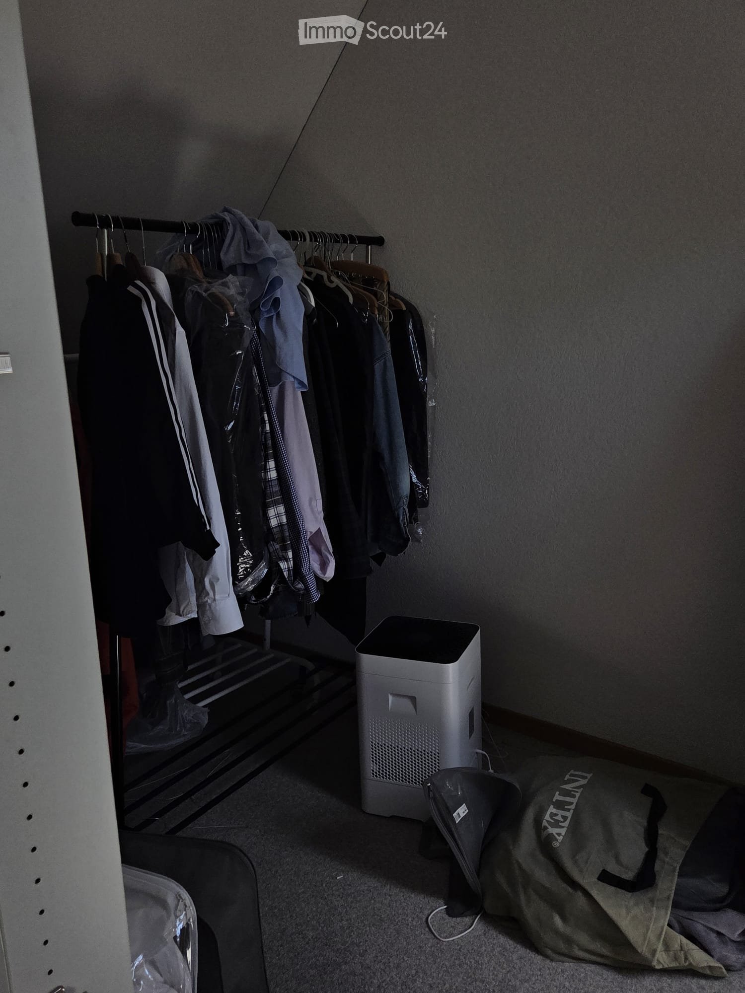 A small, furnished closet space with a wardrobe, air purifier, and a backpack on the floor.