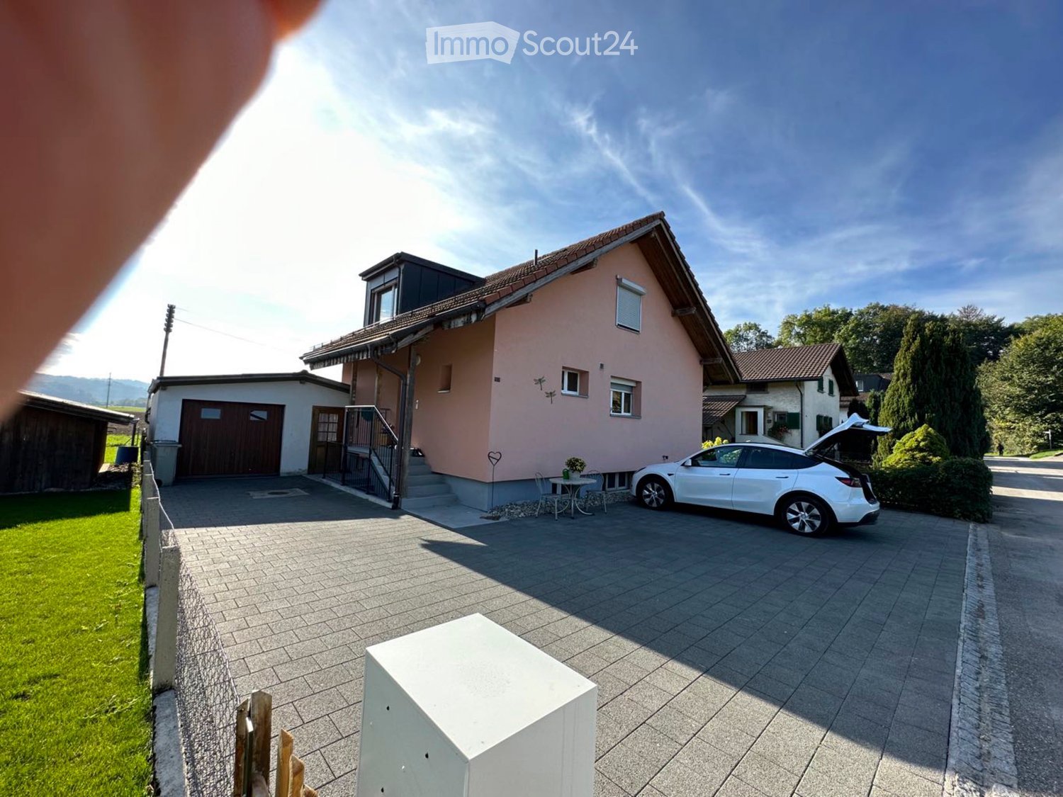 Two-story house with pink exterior, garage, driveway, and a small outdoor seating area with a table and chairs.