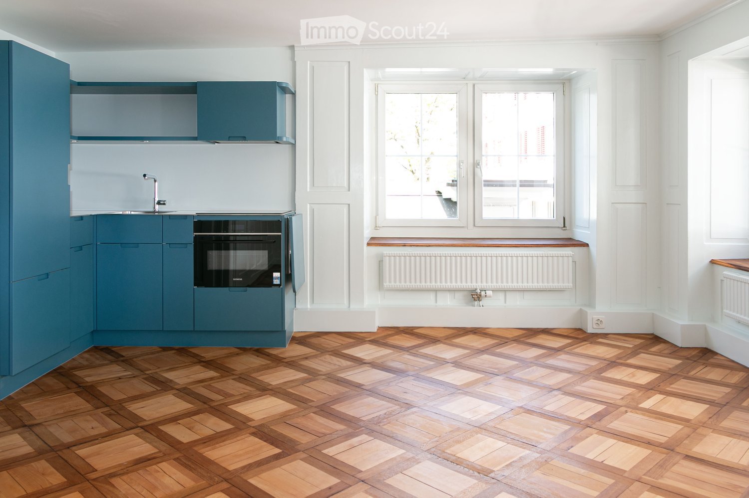 Modern kitchen with blue cabinets, a stainless steel sink, a built-in oven, and a herringbone wooden floor.