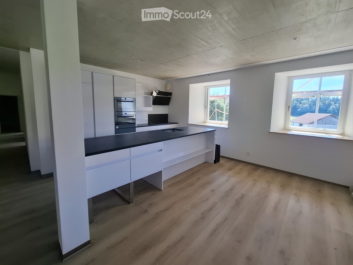 Modern kitchen with white cabinets, dark countertop, and wooden flooring. Features an island with built-in storage and an oven.