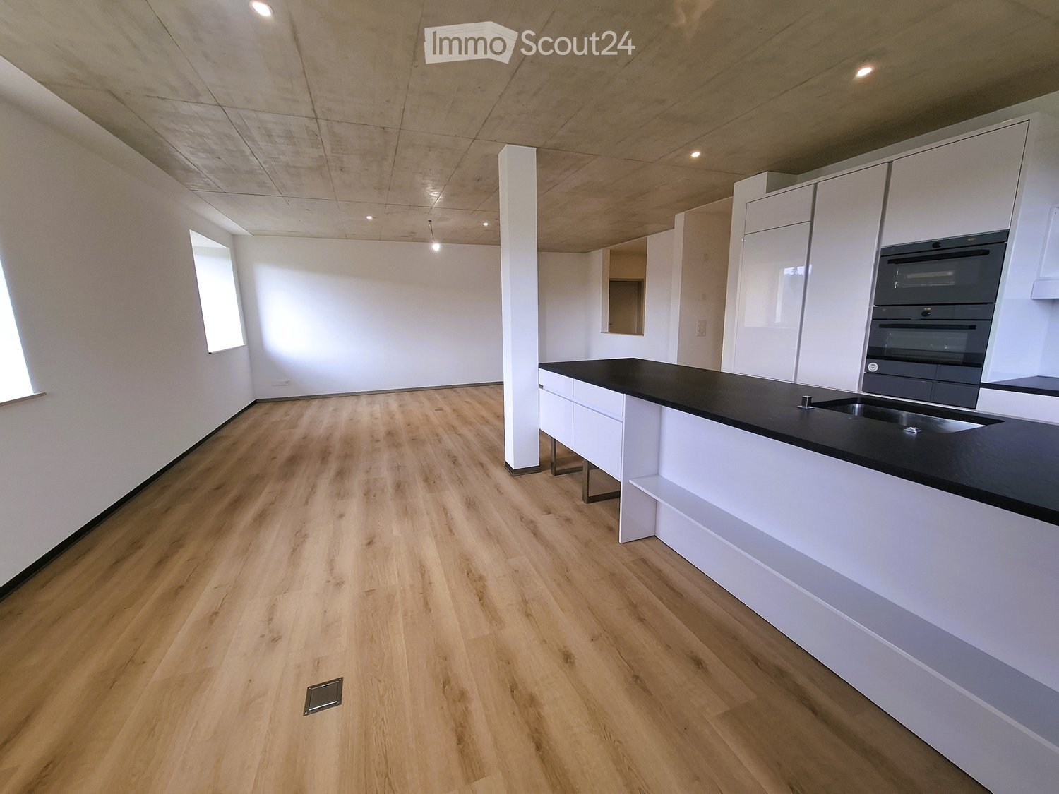 Modern kitchen with white cabinets, black countertop, and wooden flooring.