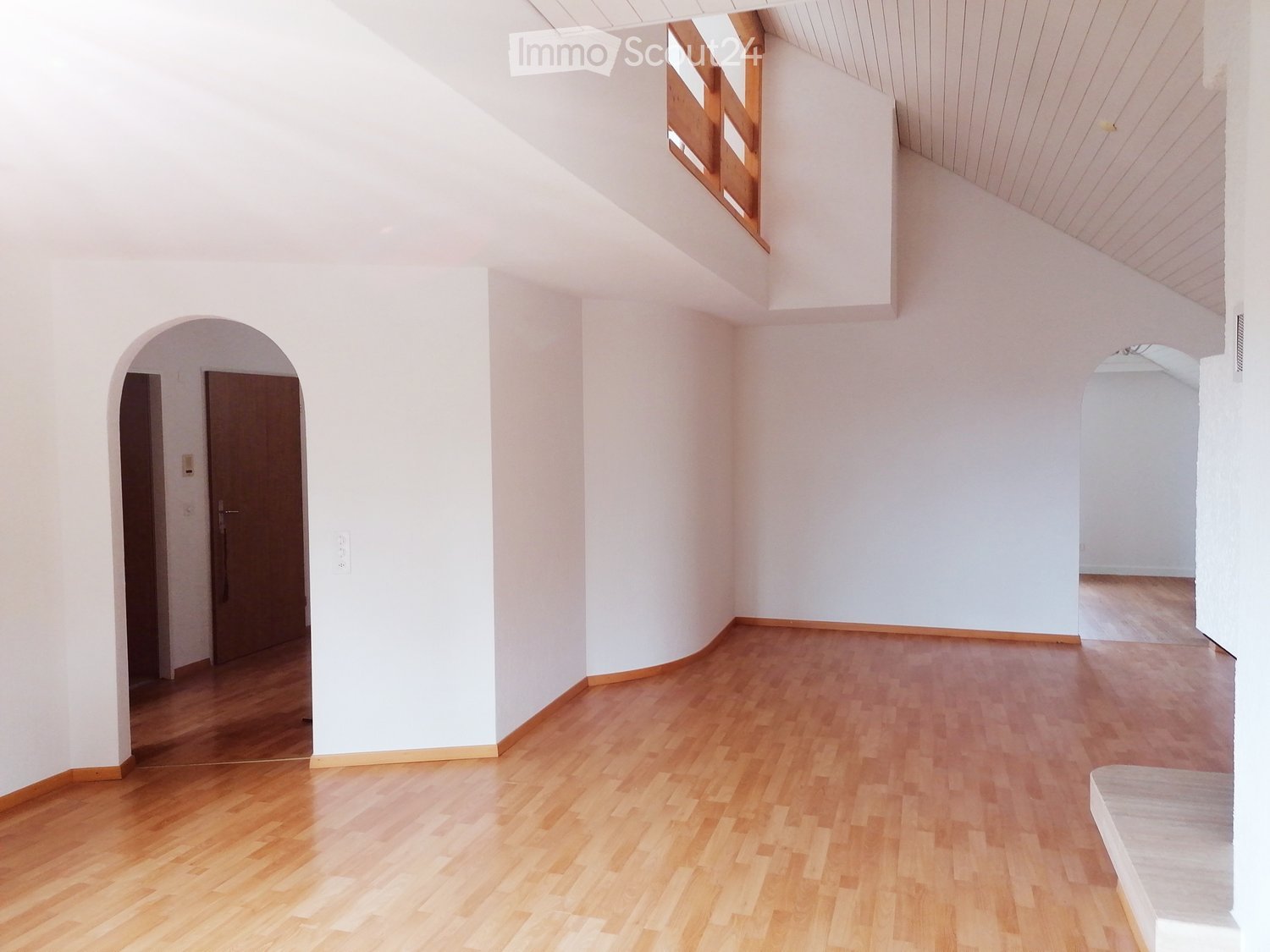 Empty room with white walls, wooden floor, and arched doorways leading to other spaces.