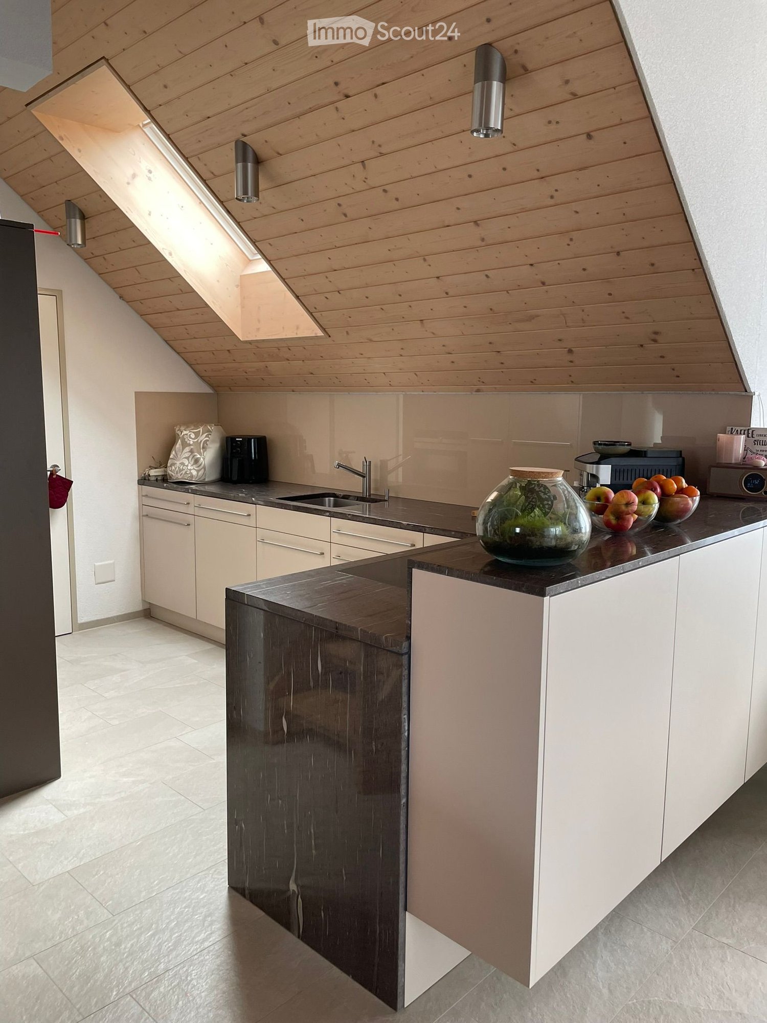 Modern kitchen with white cabinets, dark countertops, and a central island. Features include a sink, faucet, coffee maker, bowl, fruits, vase, and built-in cabinets.
