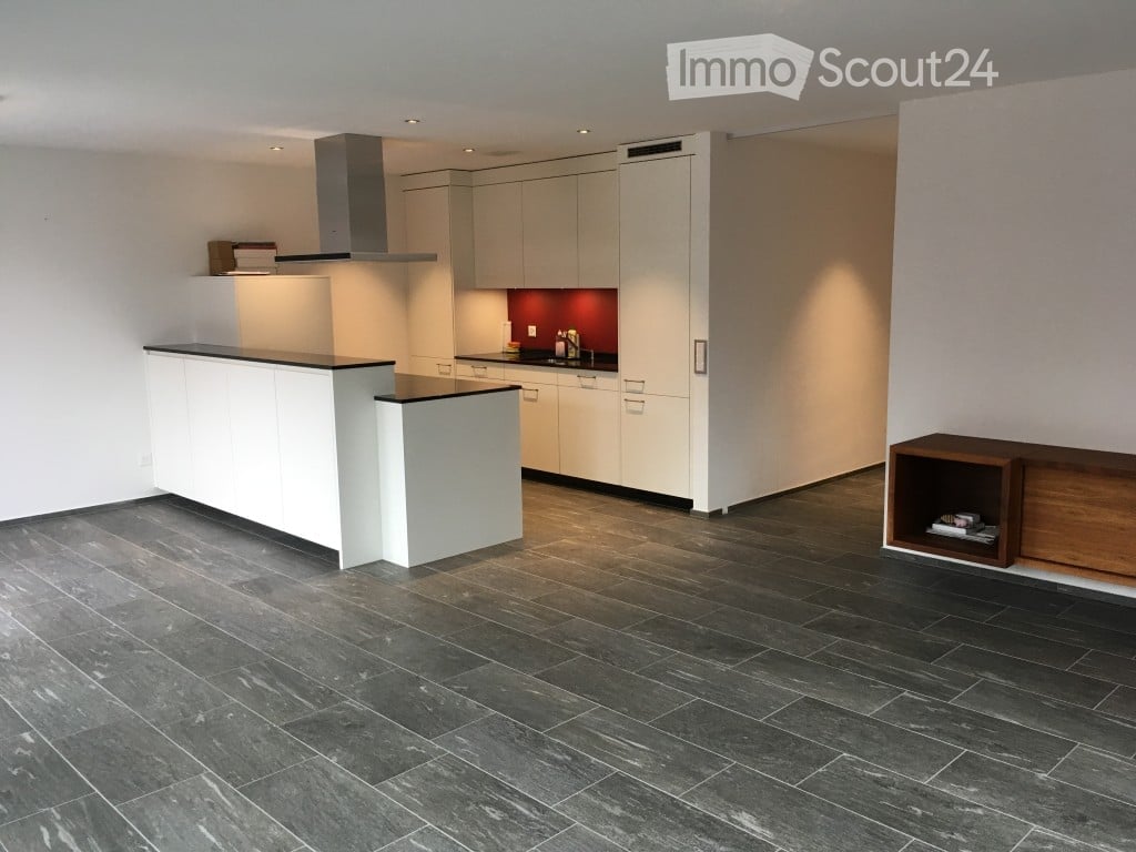 Modern kitchen with white cabinets, a central island, dark tiled floor, and a range hood. A wooden shelf is visible on the right side.