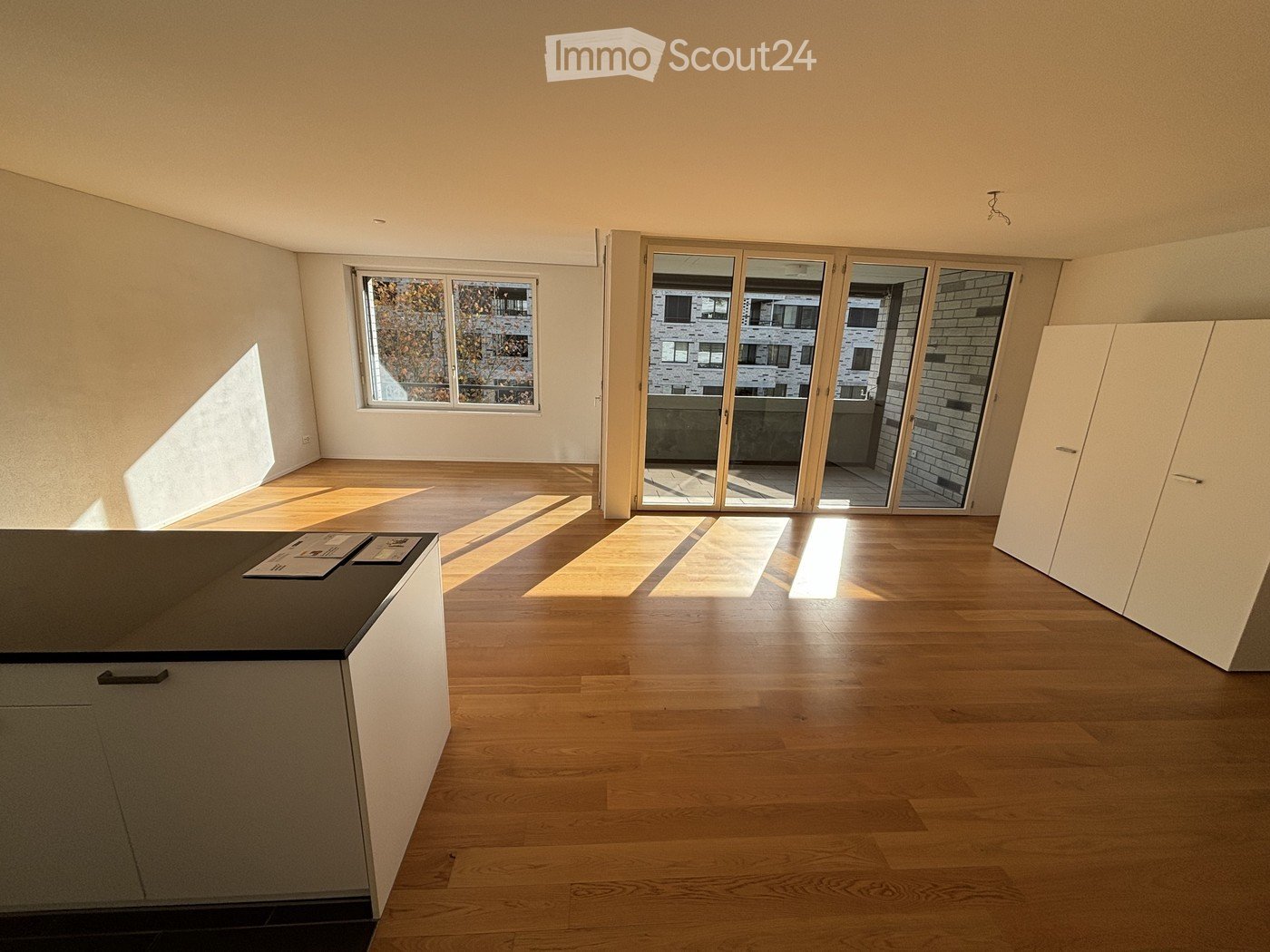 Empty room with wooden flooring, large windows, and sliding glass doors leading to a balcony. No furniture or equipment present.