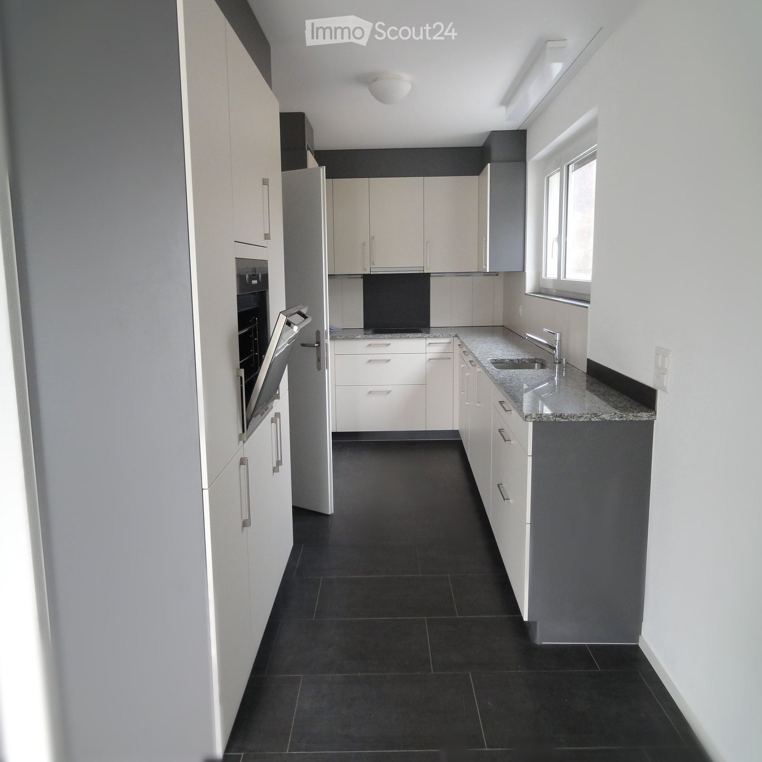 Modern kitchen with white cabinets, granite countertop, black tiled floor, and stainless steel sink and faucet.