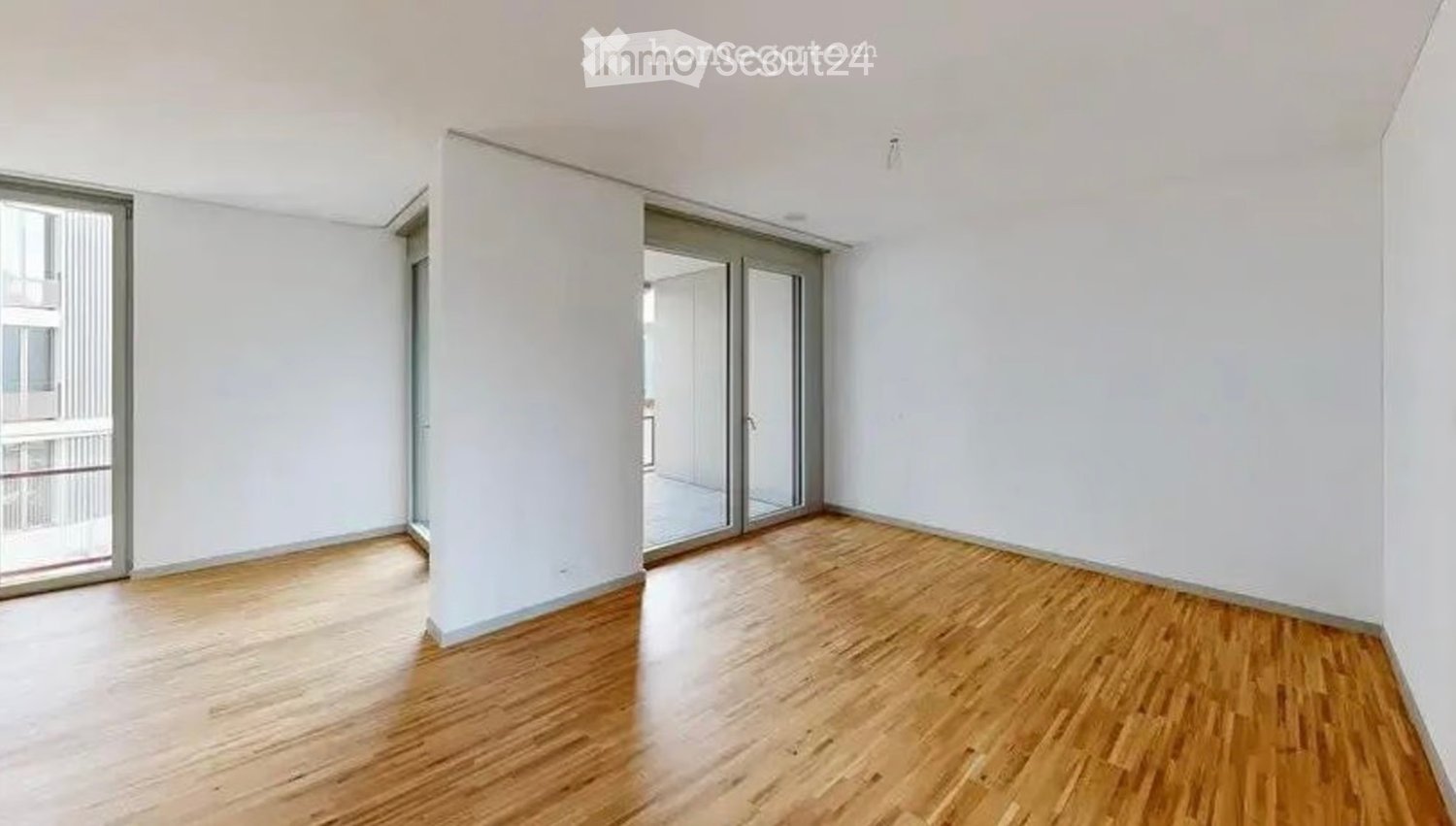 Empty room with wooden flooring, white walls, and large glass sliding doors leading to a balcony.