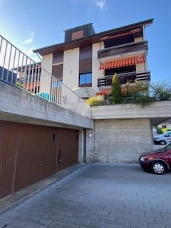 Modern multi-story apartment building with a covered garage and parking area. Features include balconies, large windows, and a clean, contemporary design.