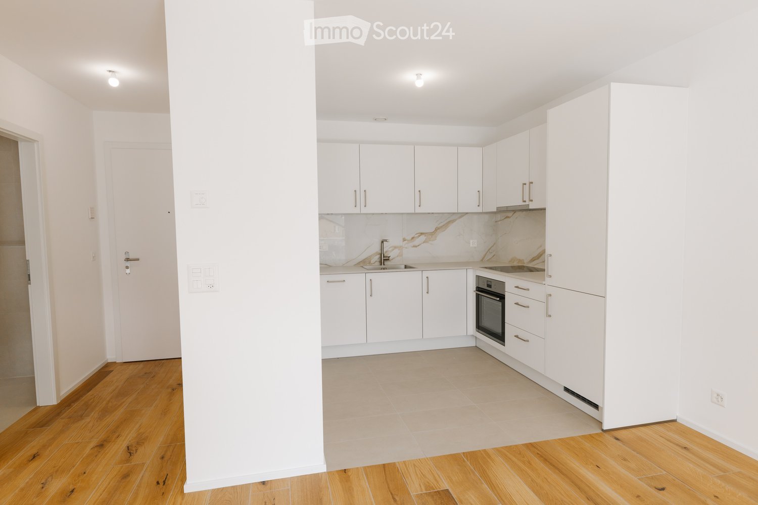 Modern kitchen with white cabinets, marble backsplash, and wooden flooring.