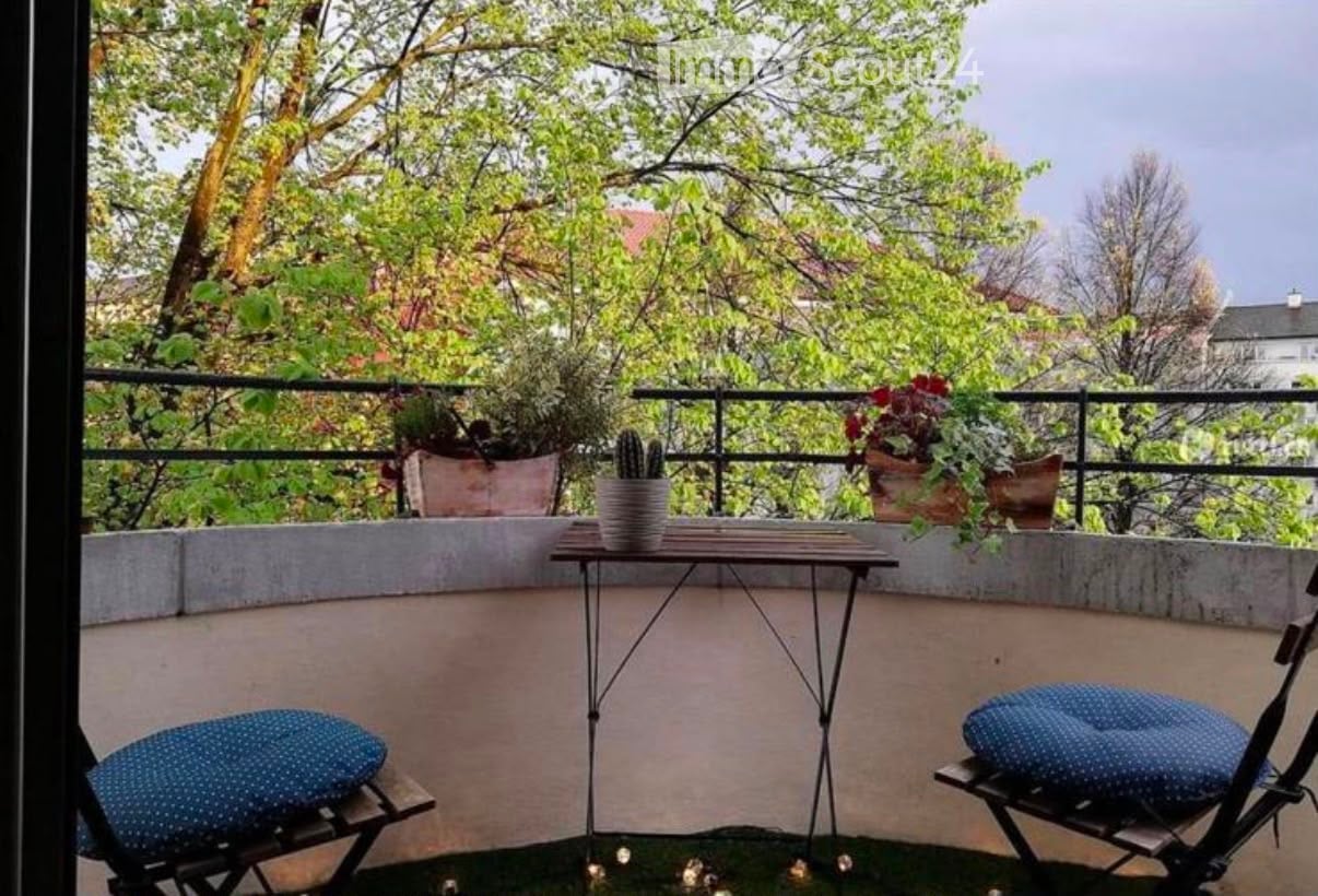 Balcony with a small table, two chairs, and potted plants, surrounded by greenery and trees.