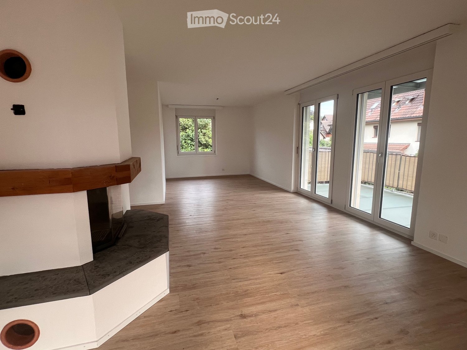 Empty room with wooden flooring, white walls, large sliding glass doors leading to a balcony, and a fireplace with a wooden mantel.