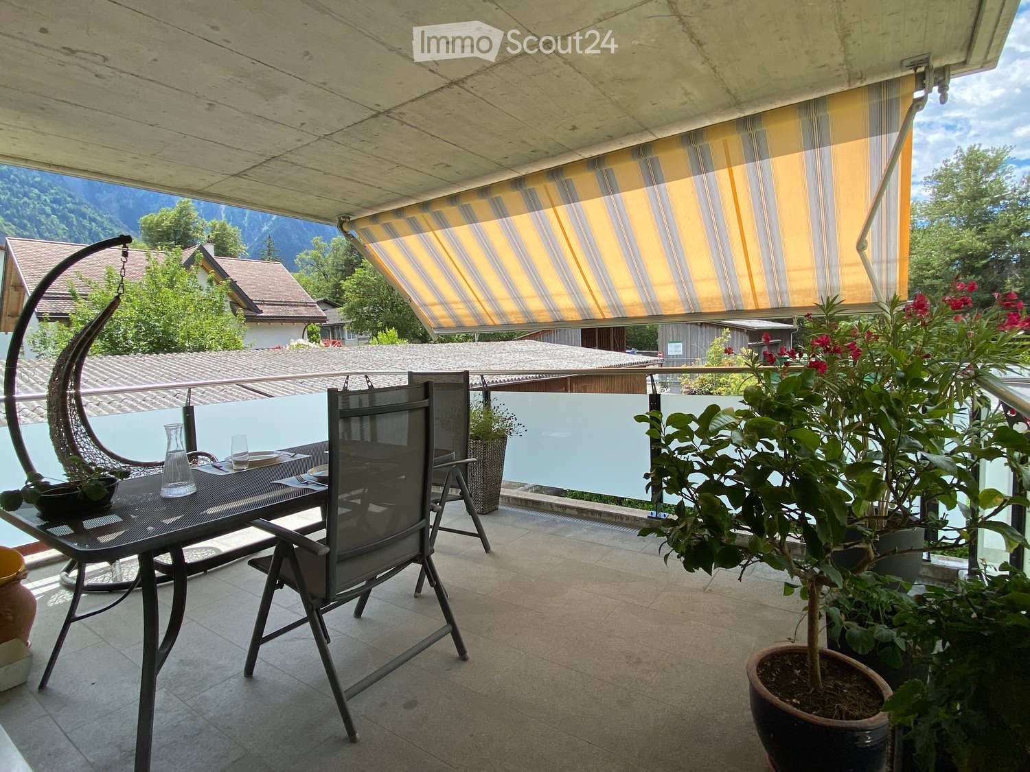 Balcony with a table, chairs, potted plants, and a scenic mountain view.