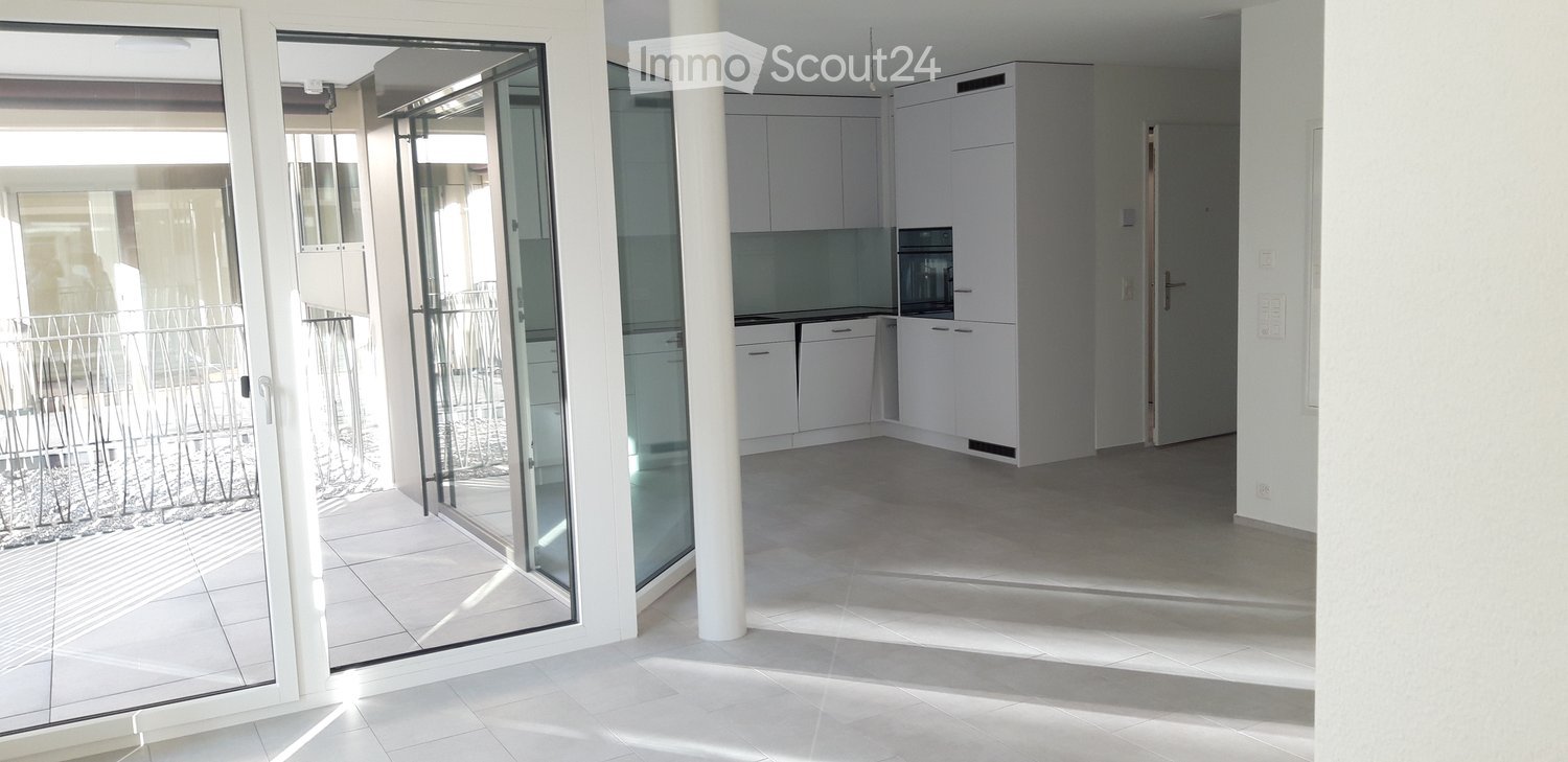 Empty kitchen with white cabinets, a microwave, and a tiled floor, connected to a balcony through large glass doors.