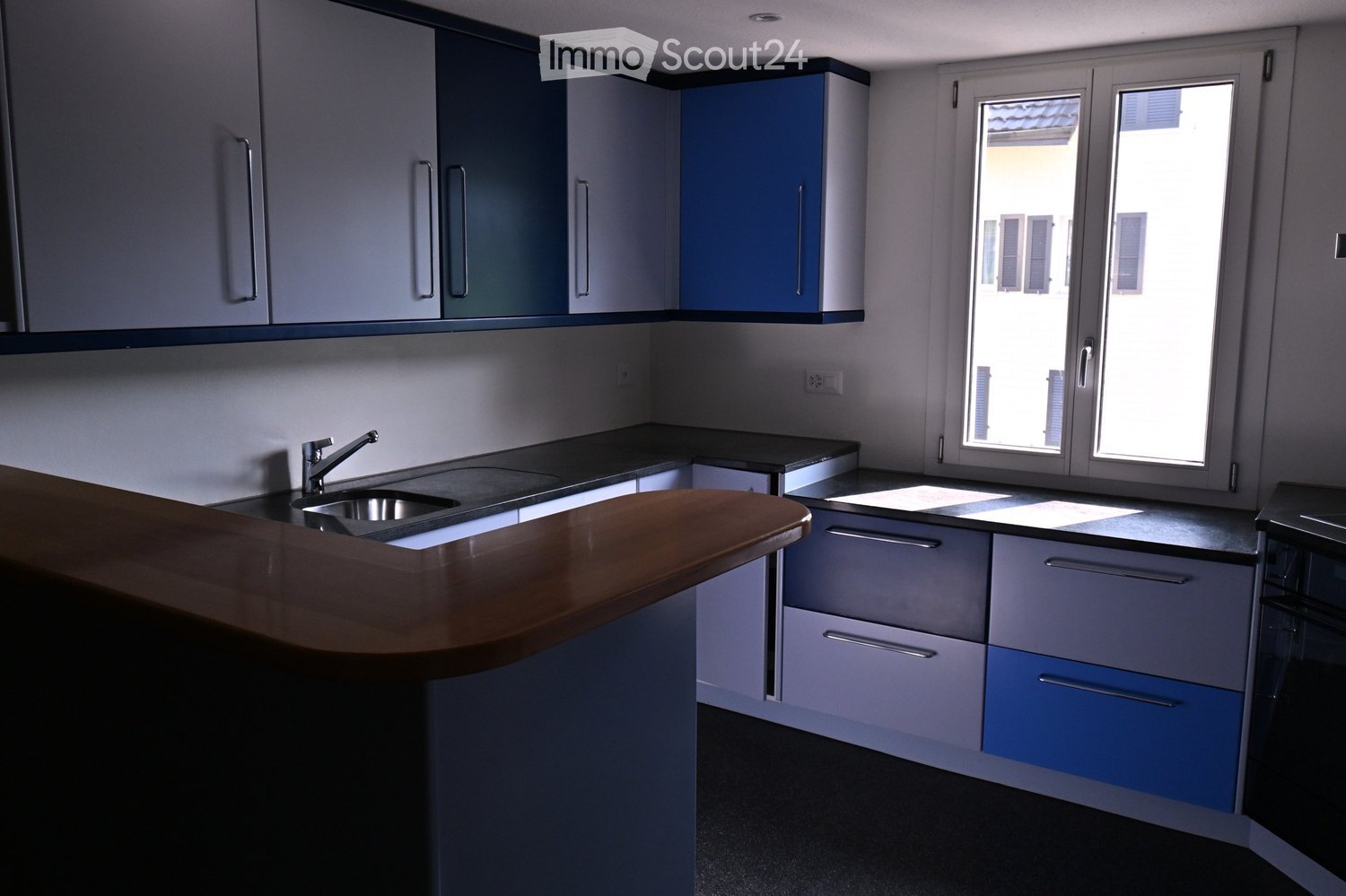 Modern kitchen with grey and blue cabinets, a wooden countertop, and a stainless steel sink.