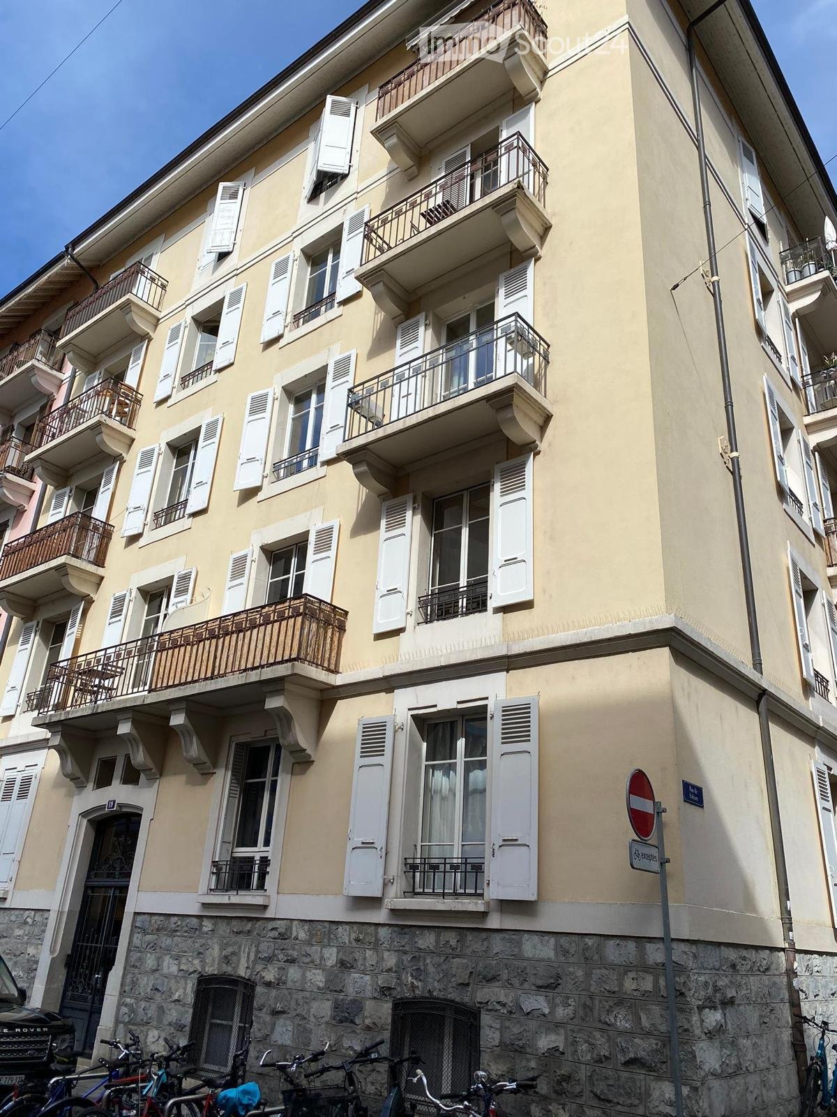 Four-story residential building with light yellow facade, multiple windows with white shutters, and balconies with metal railings.
