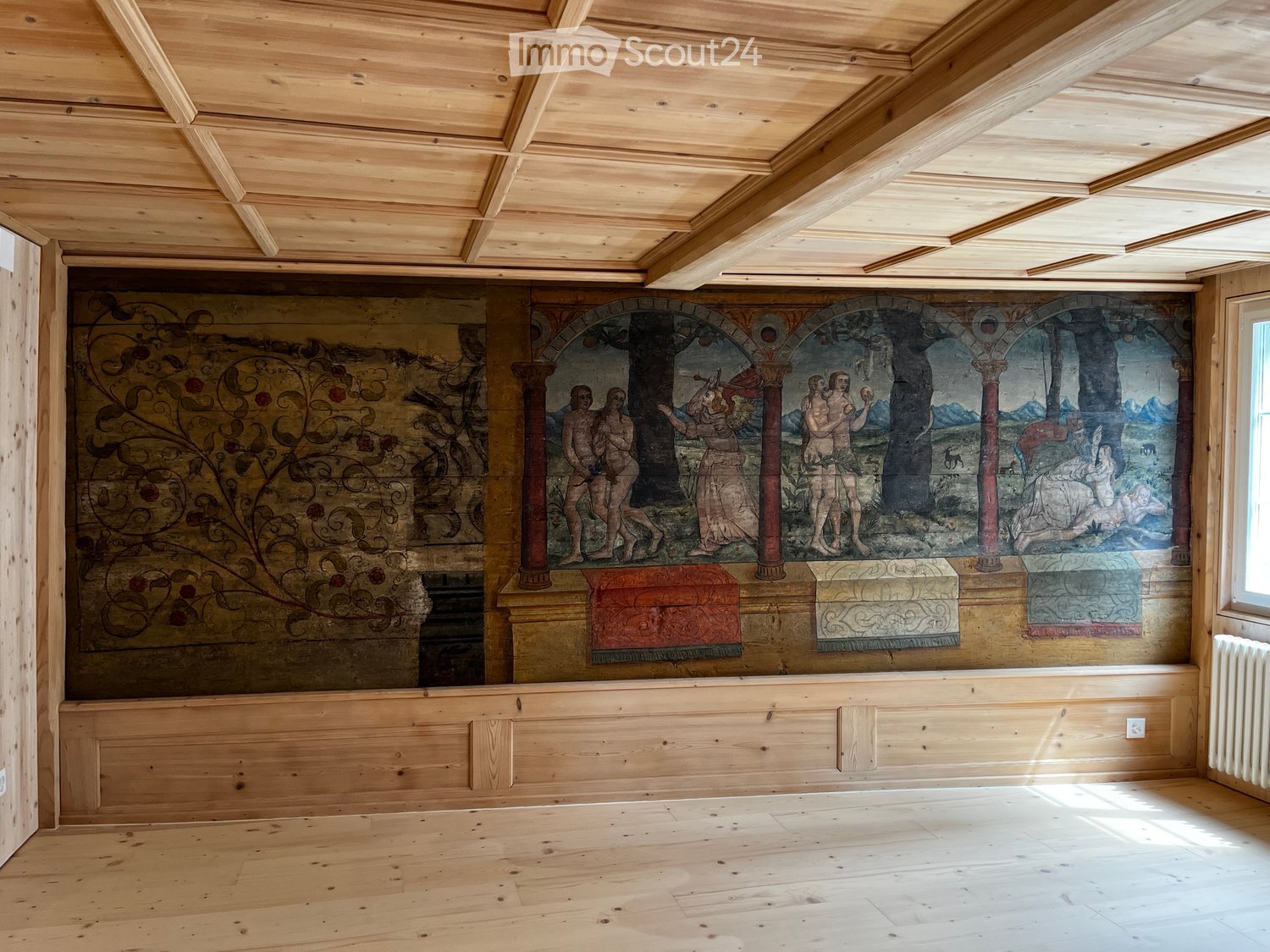 An unfurnished room with wooden walls, a painted mural, and a wooden ceiling. The room is empty, with no furniture or furnishings visible.