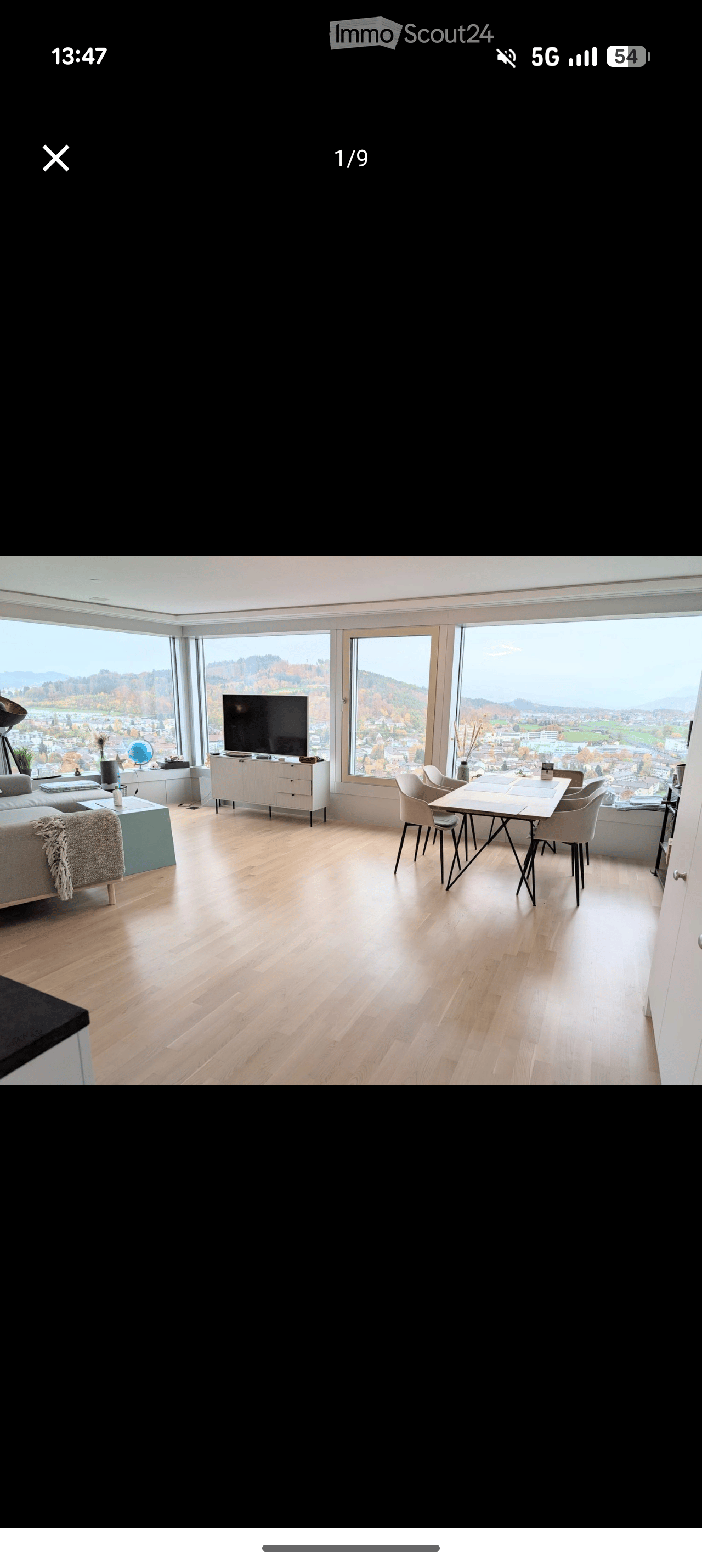 Modern living and dining area with large windows offering a scenic view, featuring a sofa, coffee table, television, dining table, and chairs.
