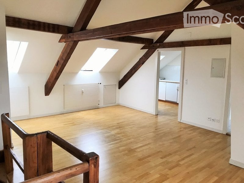Empty attic room with wooden beams, wooden flooring, and skylights. No furniture or equipment present.
