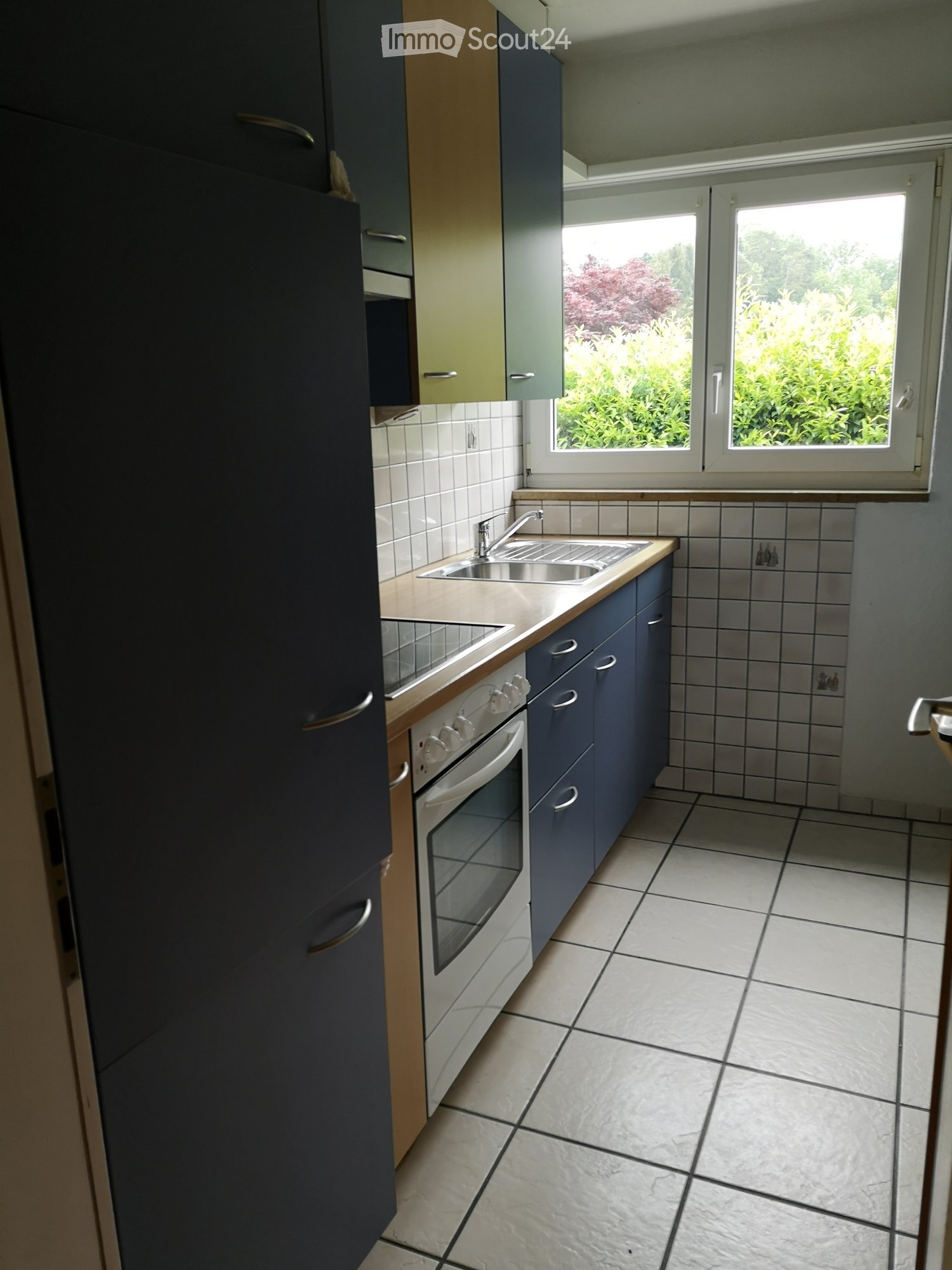 Modern kitchen with dark blue cabinets, white tiles, and a window overlooking greenery.