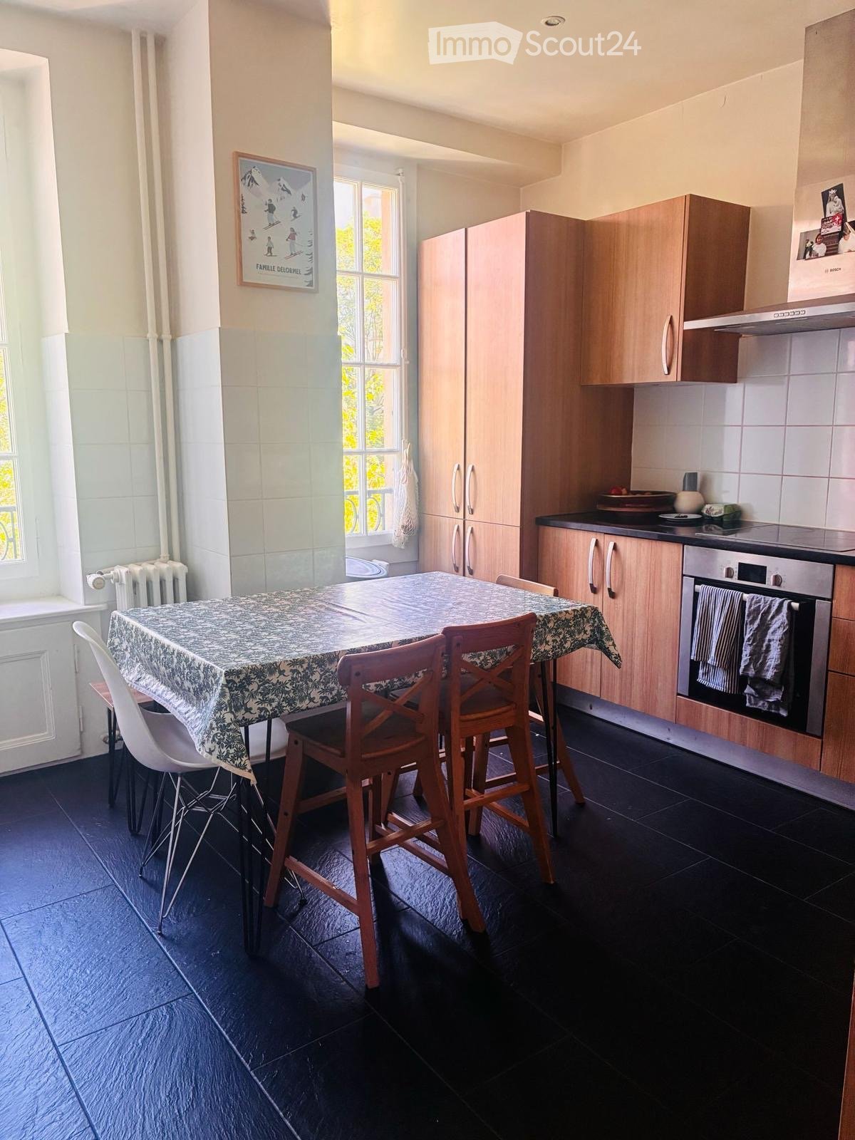 A modern kitchen with wooden cabinets, a black countertop, and a dining area featuring a table and chairs.