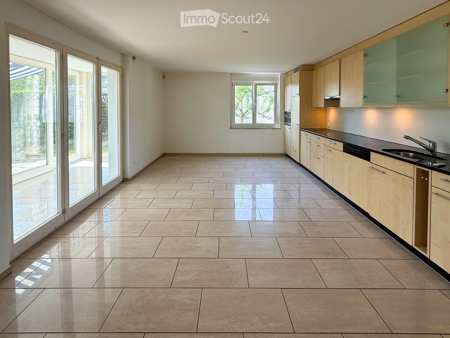 Empty kitchen with light wooden cabinets, black countertops, and large sliding glass doors leading to an outdoor area.