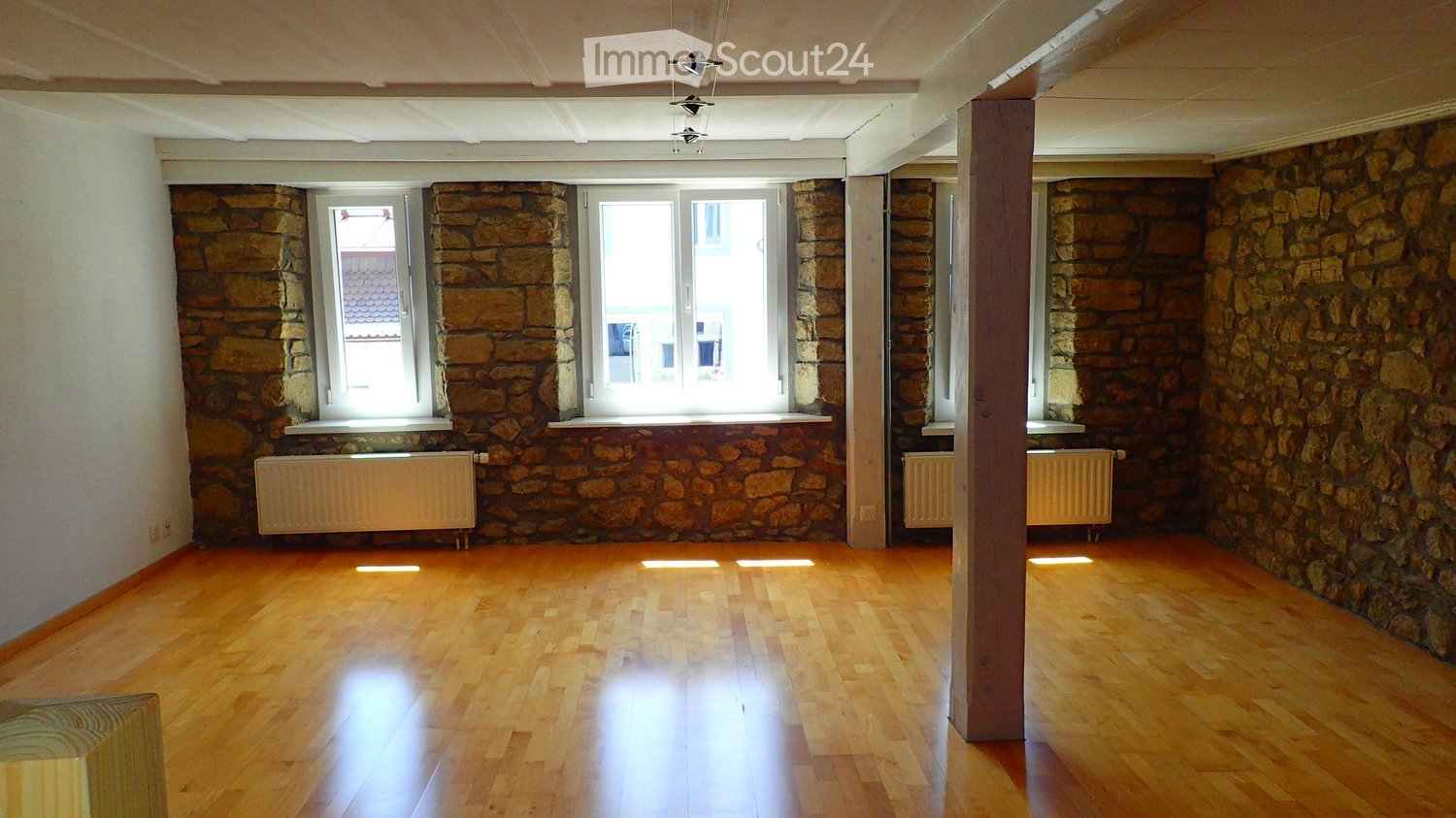 Empty room with wooden flooring, stone walls, and large windows. No furniture or equipment present.
