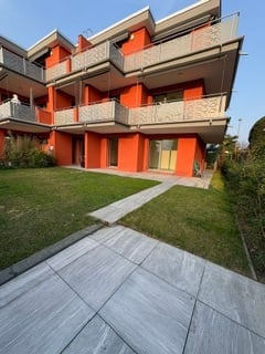Modern orange apartment building with multiple balconies and a well-maintained lawn in front.