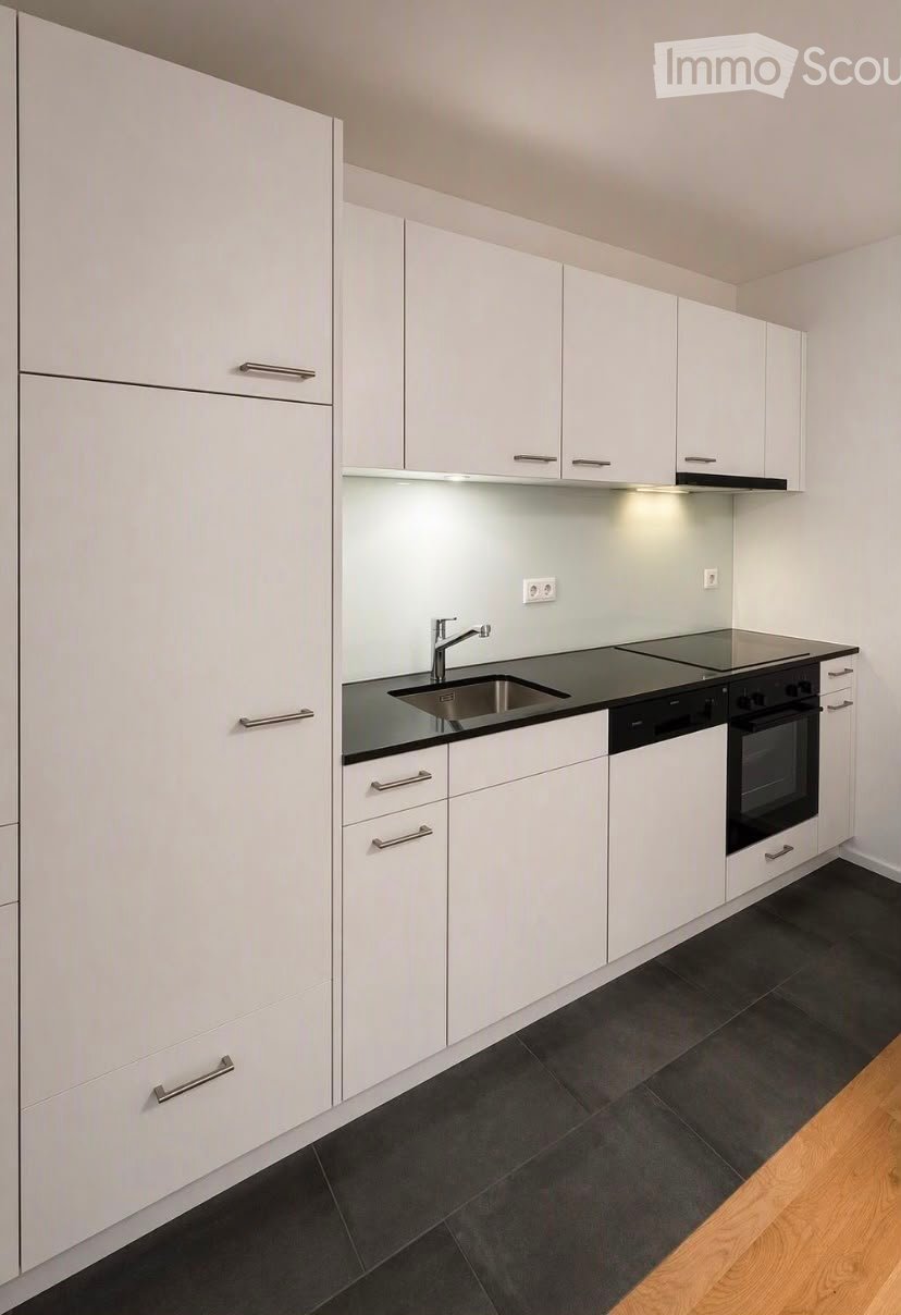 Modern kitchen with white cabinets, black countertops, stainless steel sink and faucet, built-in stove and oven, and dark tiled flooring.