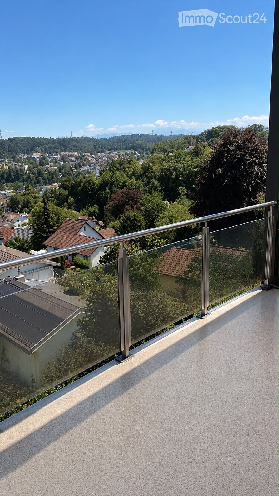 Balcony with glass railing and metal balustrade, overlooking a suburban area with houses and trees.