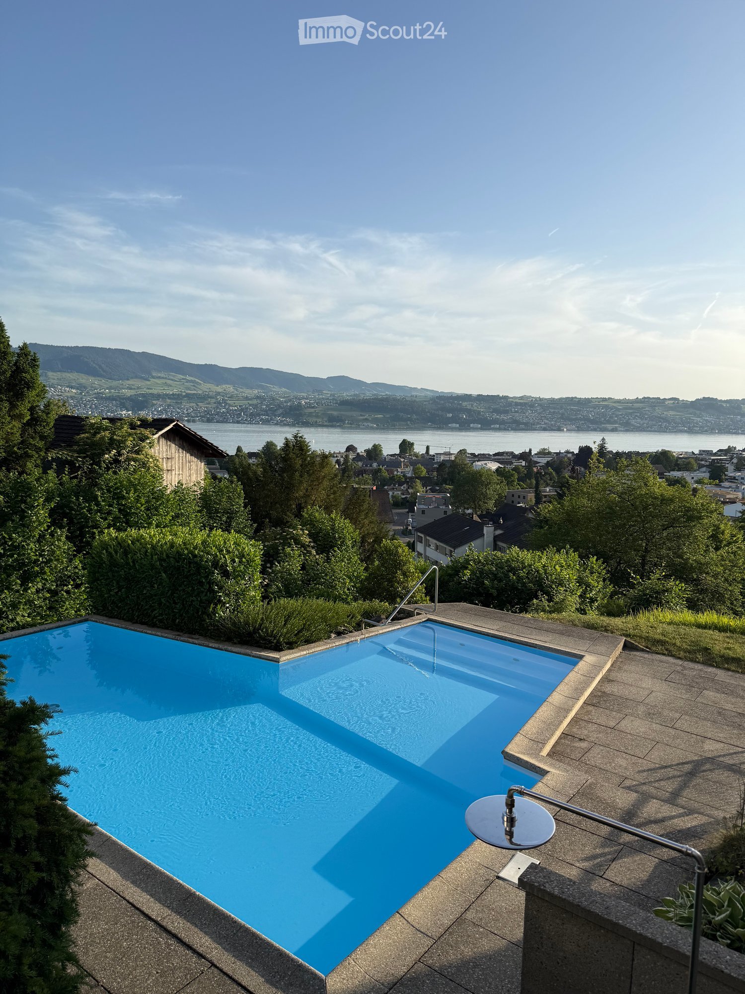 A modern swimming pool on a rooftop terrace with a scenic view of a lake and distant mountains.