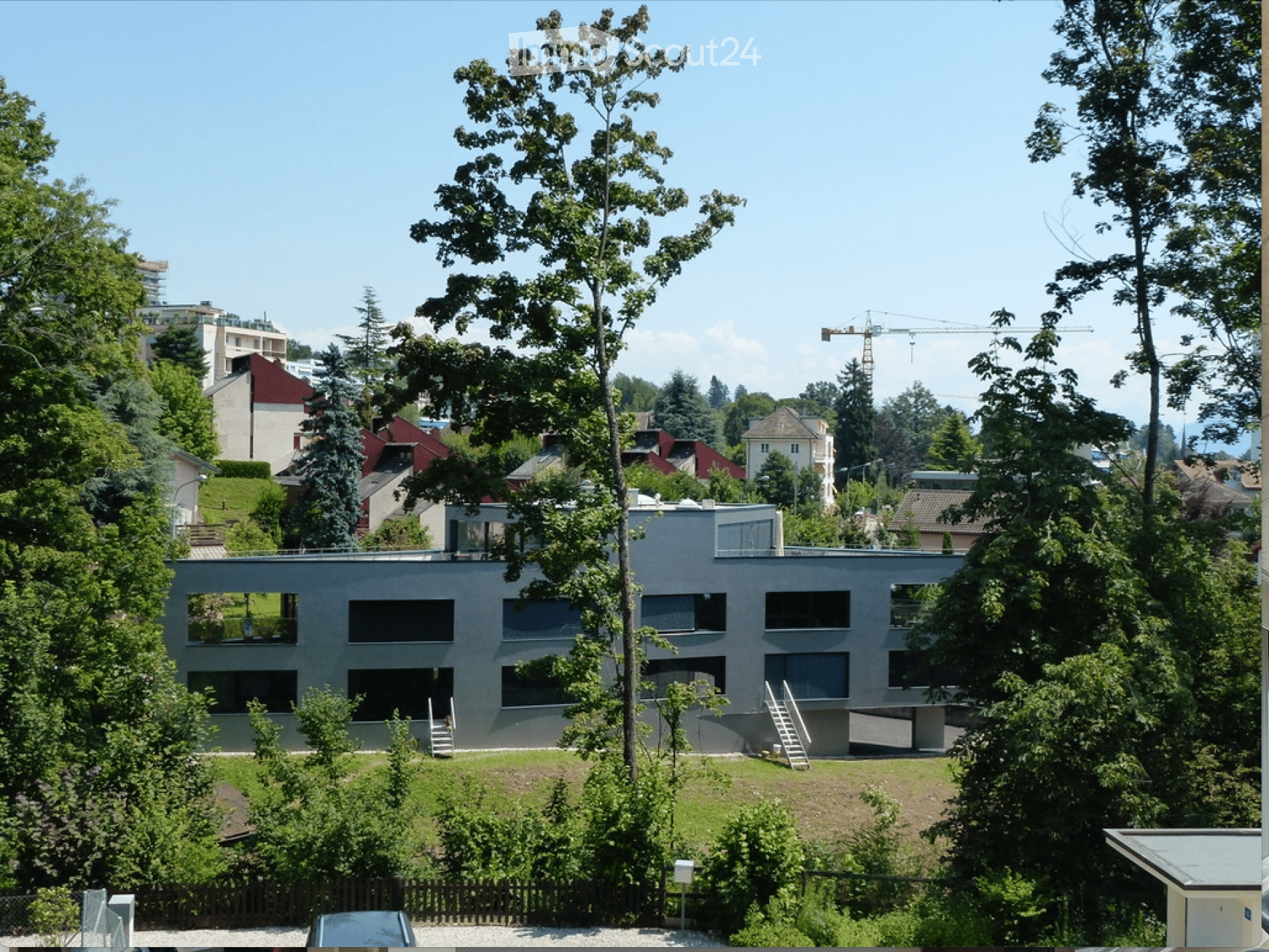 Modern two-story building with large windows and a flat roof, surrounded by trees and greenery.