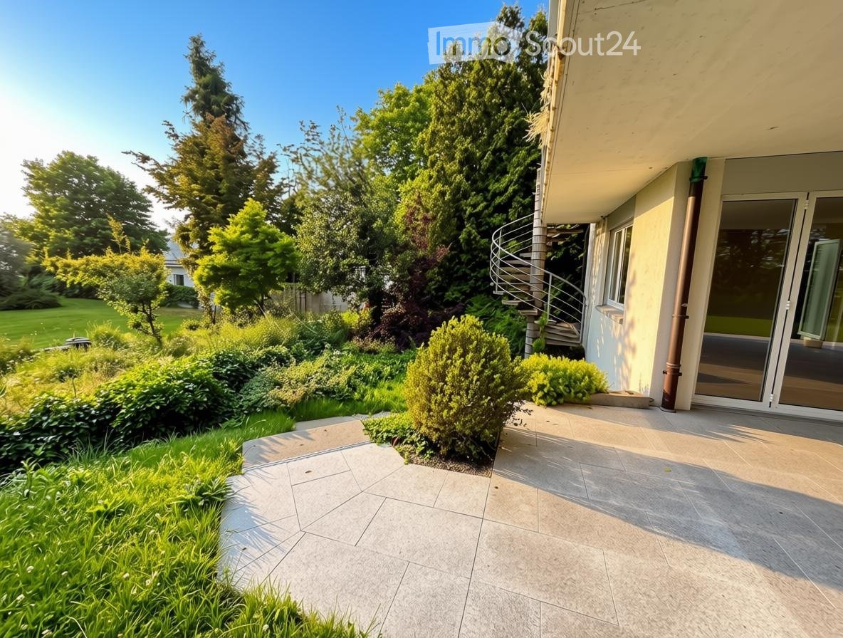 Well-maintained garden with a variety of trees, shrubs, and a paved patio area adjacent to a house with a spiral staircase leading to an upper level.