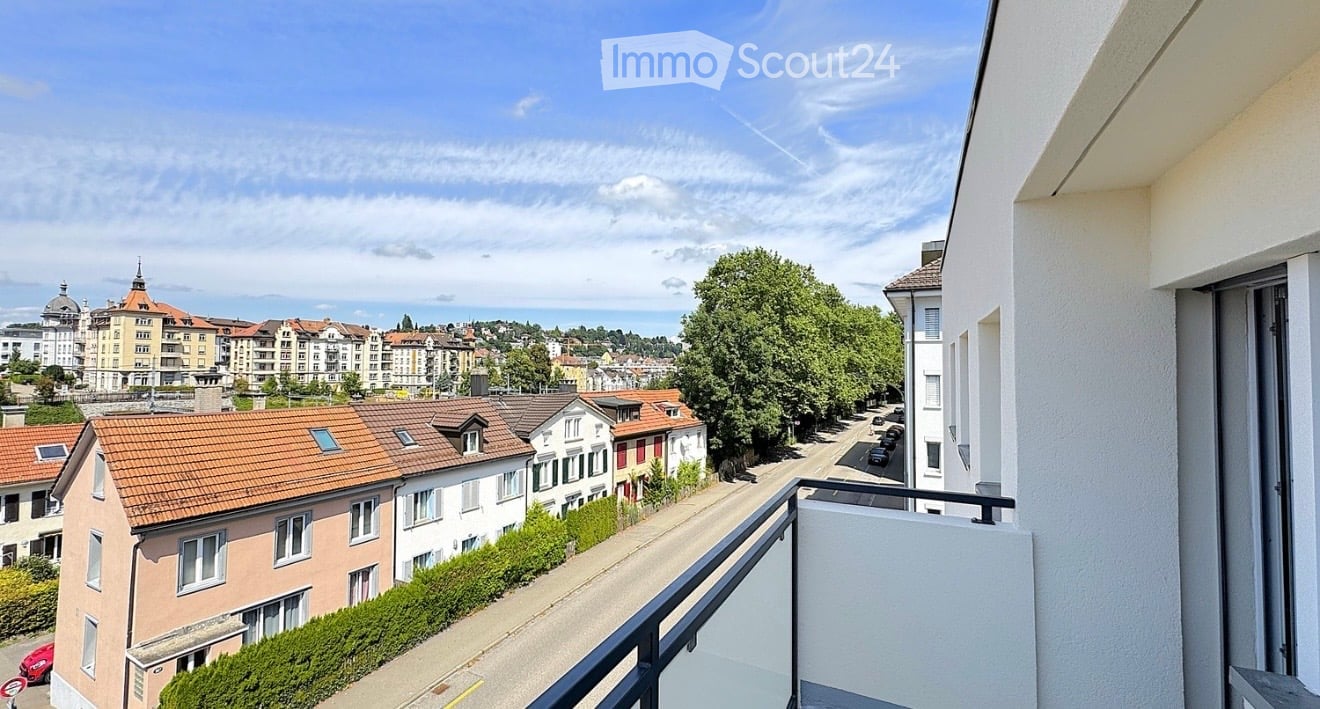 Balcony overlooking a cityscape with residential buildings, trees, and a clear blue sky.