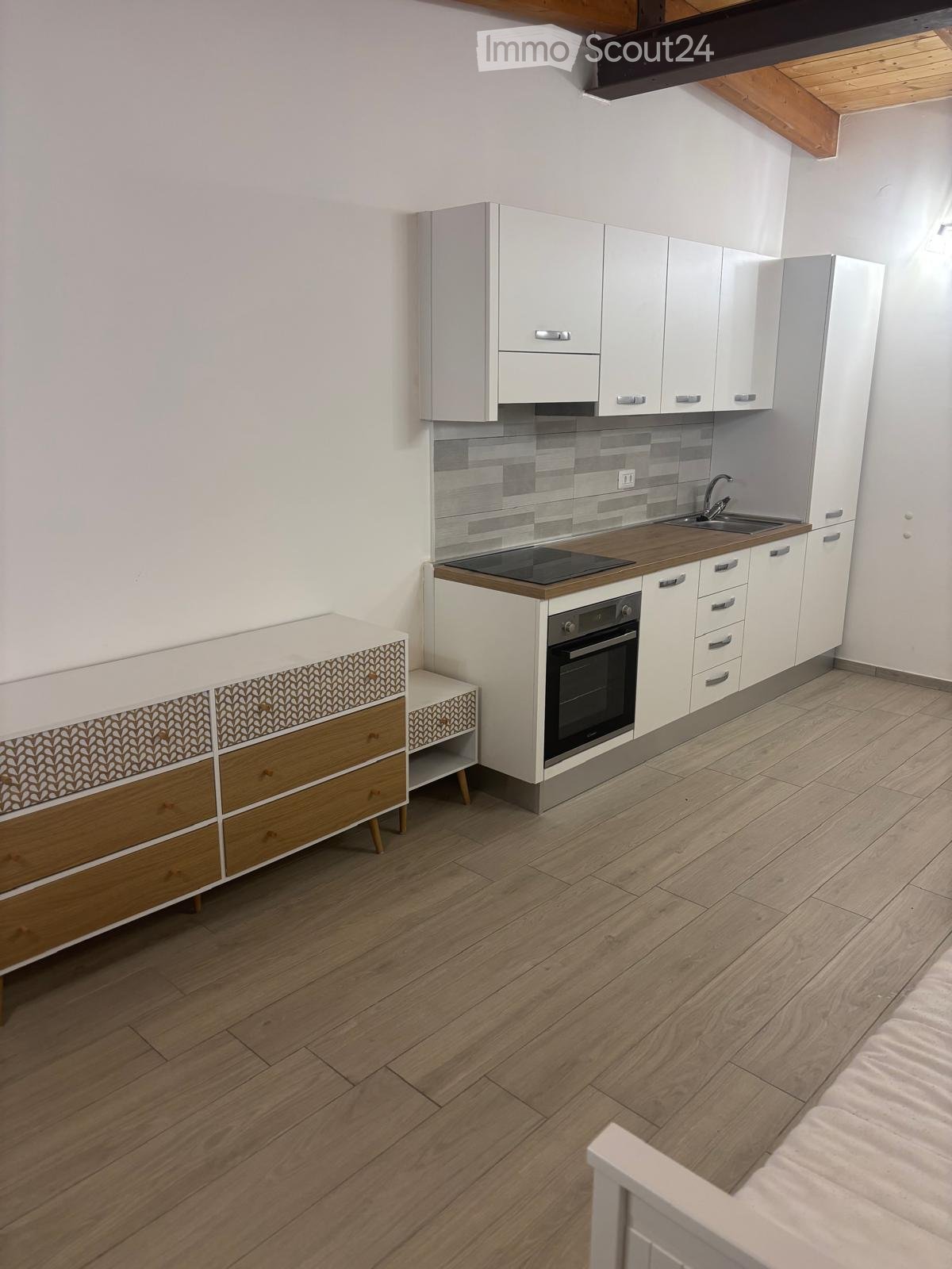 Modern kitchen with white cabinets, wooden countertops, and a built-in oven. Features a sink with a modern faucet and a small wooden side table with drawers.