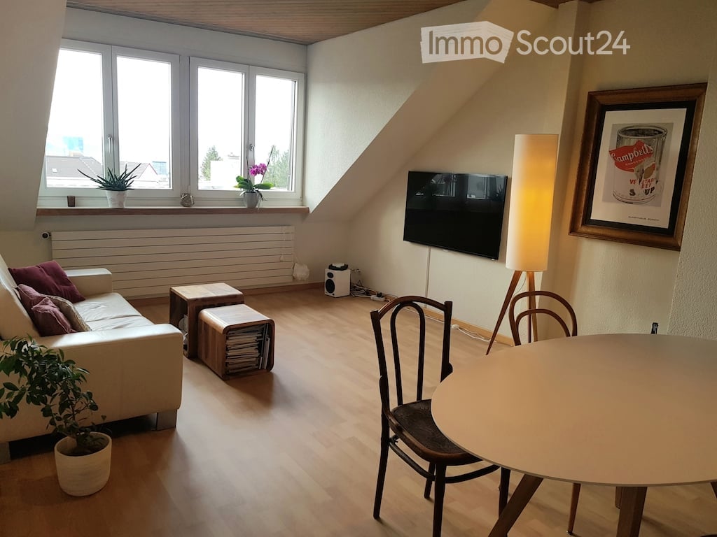 Bright living room with wooden flooring, large windows, a white sofa, a round dining table with chairs, a floor lamp, a television, and decorative plants.