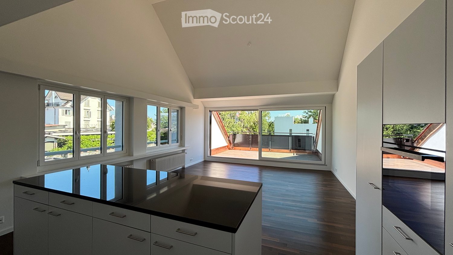 Bright, modern kitchen with white cabinets, black countertop, and large windows overlooking a balcony.