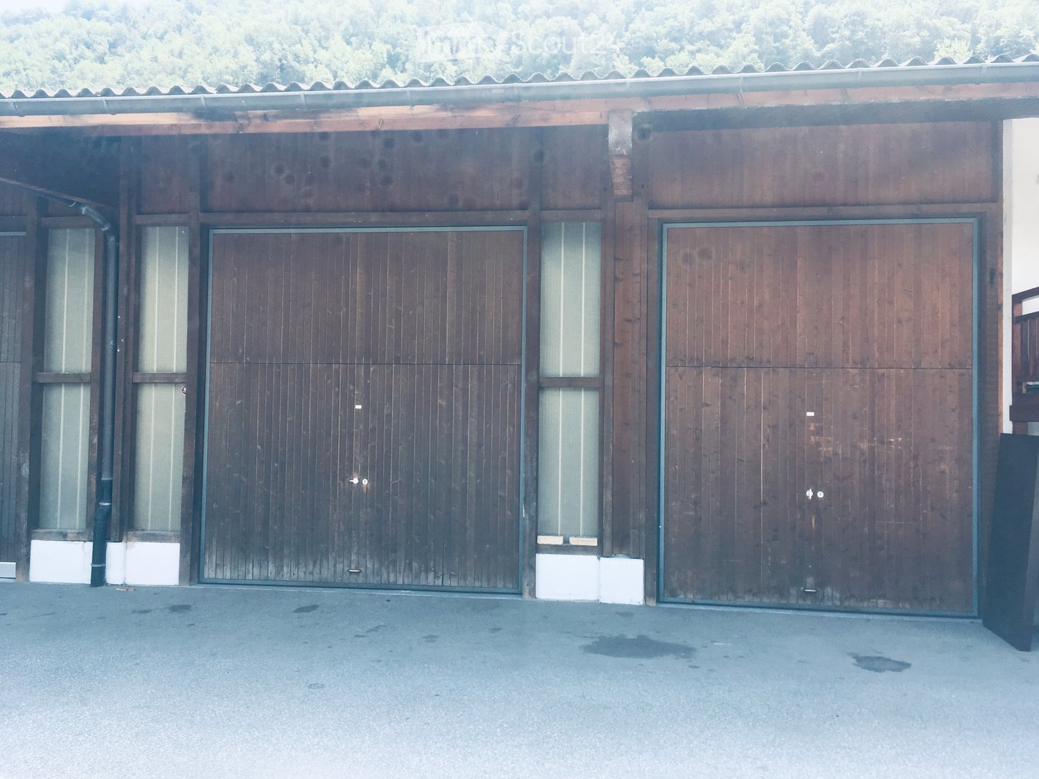 Wooden building with large garage doors and small windows, situated on a paved surface.