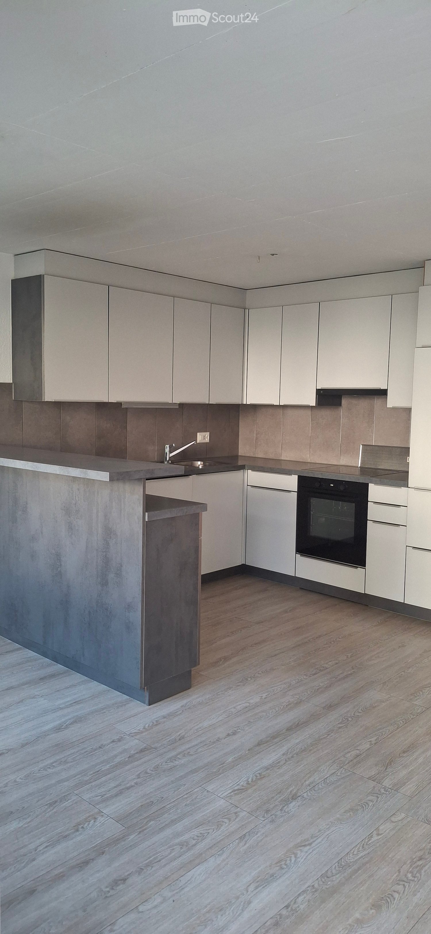 Modern kitchen with light grey cabinets, a central island, and wooden flooring. Features include a sink, faucet, oven, and dishwasher.