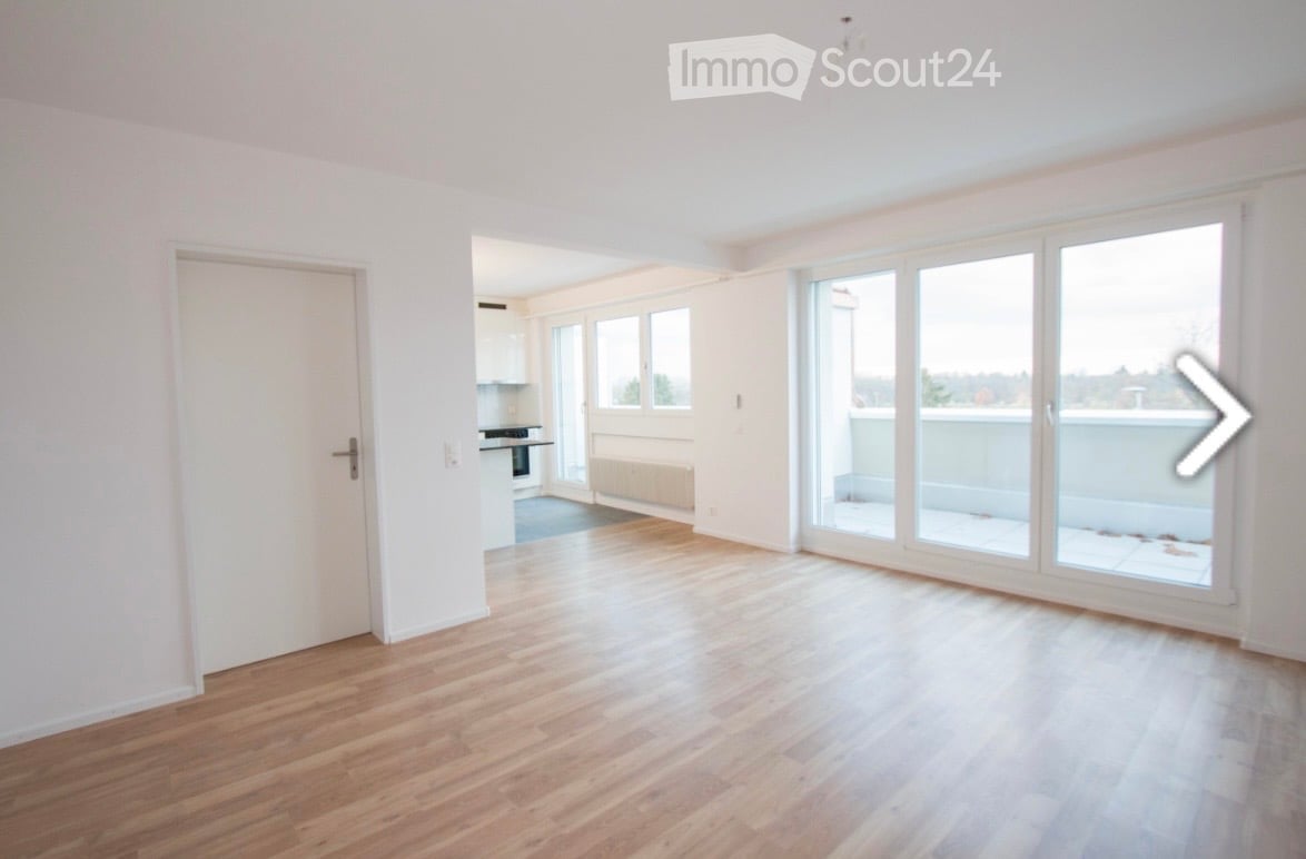 Bright, unfurnished living space with wooden flooring, large windows, and a sliding glass door leading to a balcony.