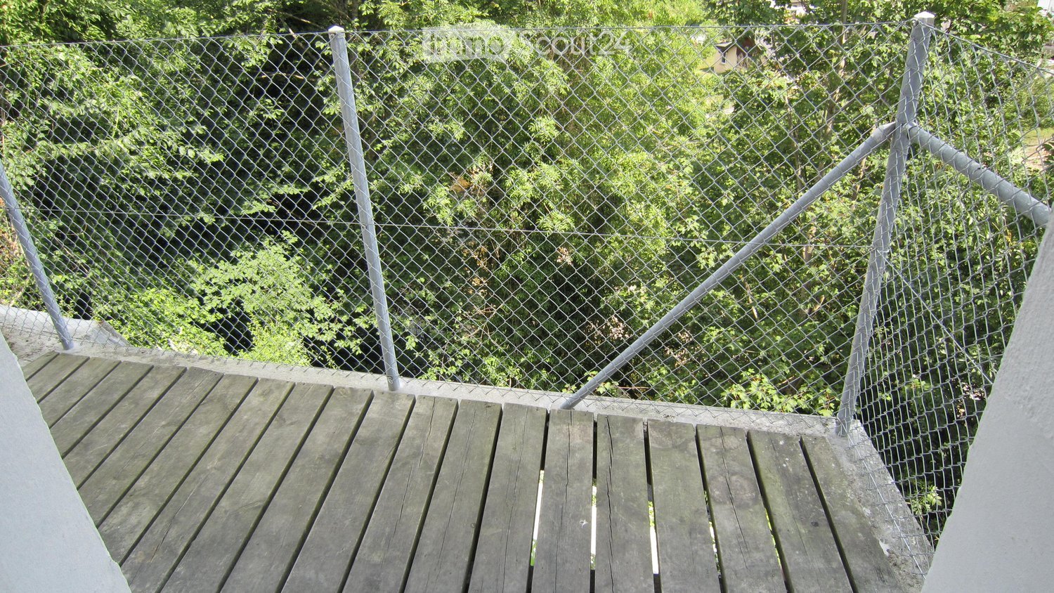 Wooden balcony with a metal safety fence, overlooking a lush green garden area.
