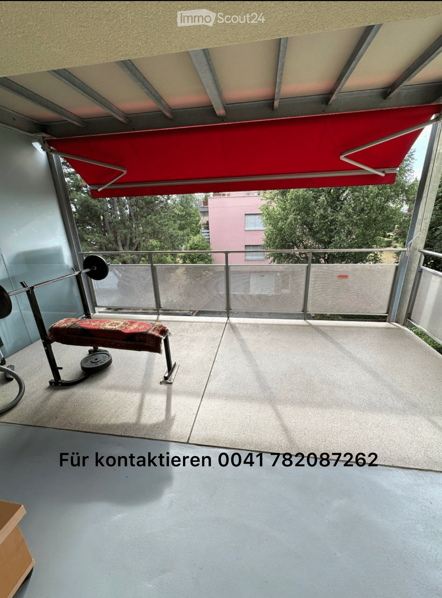 Balcony with a red awning, metal railing, and a small exercise bench with weights.