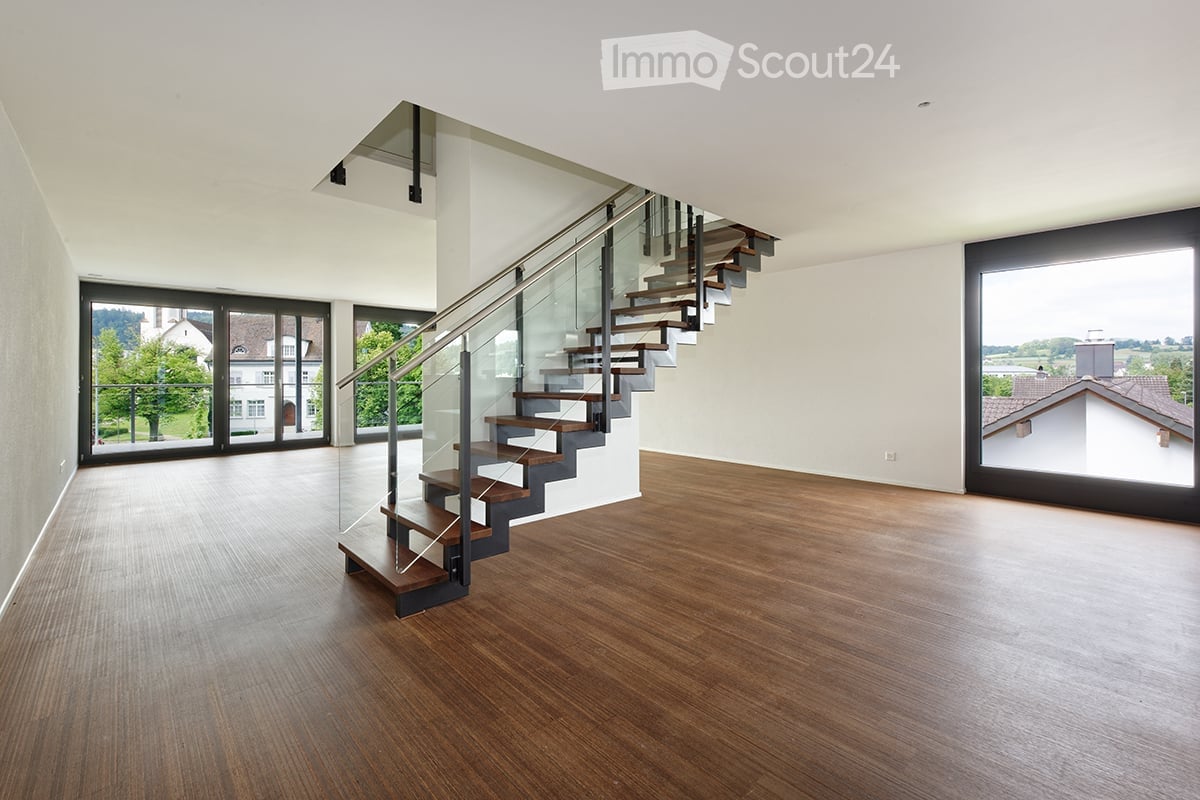 Modern hallway with wooden flooring, glass staircase, large windows, and open space.