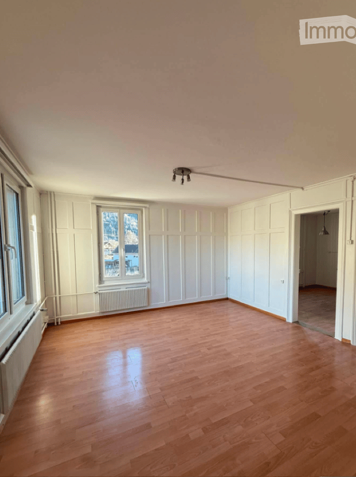 Empty room with wooden flooring, white walls, and large windows offering a view of the outside. No furniture or equipment is present.