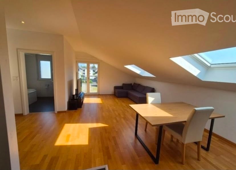 Bright, open loft-style room with wooden flooring, skylights, a sofa, a dining table with chairs, and a TV stand near the door.
